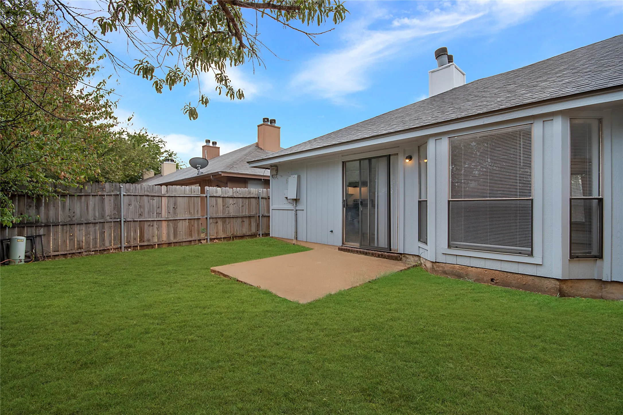 Expansive green lawn with a privacy fence, concrete patio, sliding glass door, and a bay window
