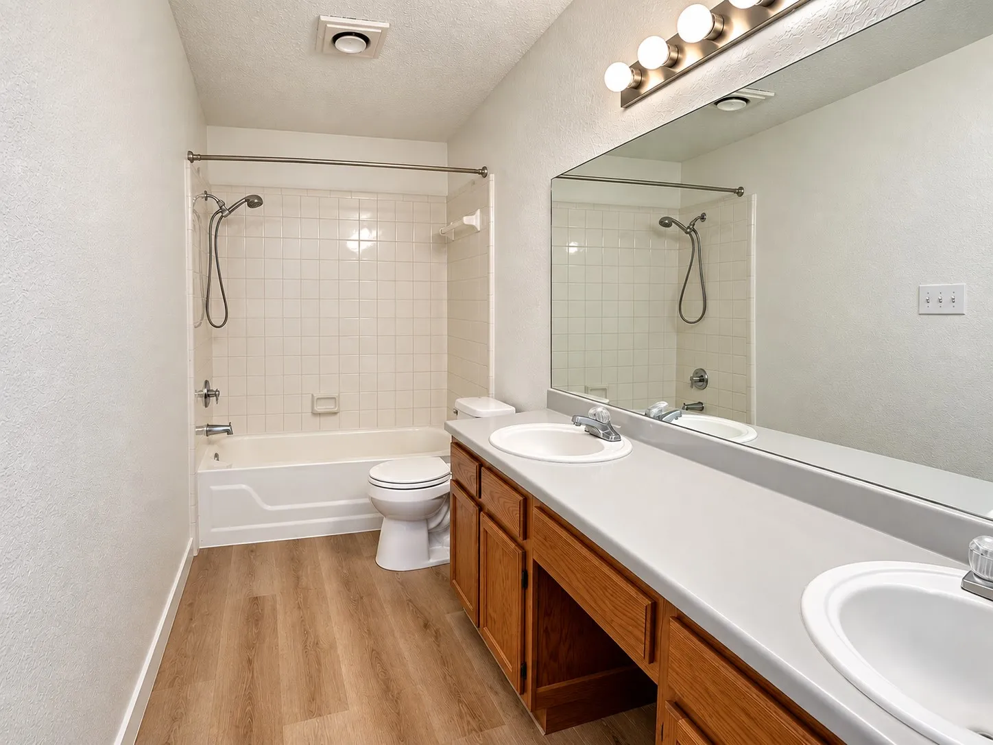 Bathroom featuring wood-finish flooring, a double vanity with integrated sinks, and a full-width mirror