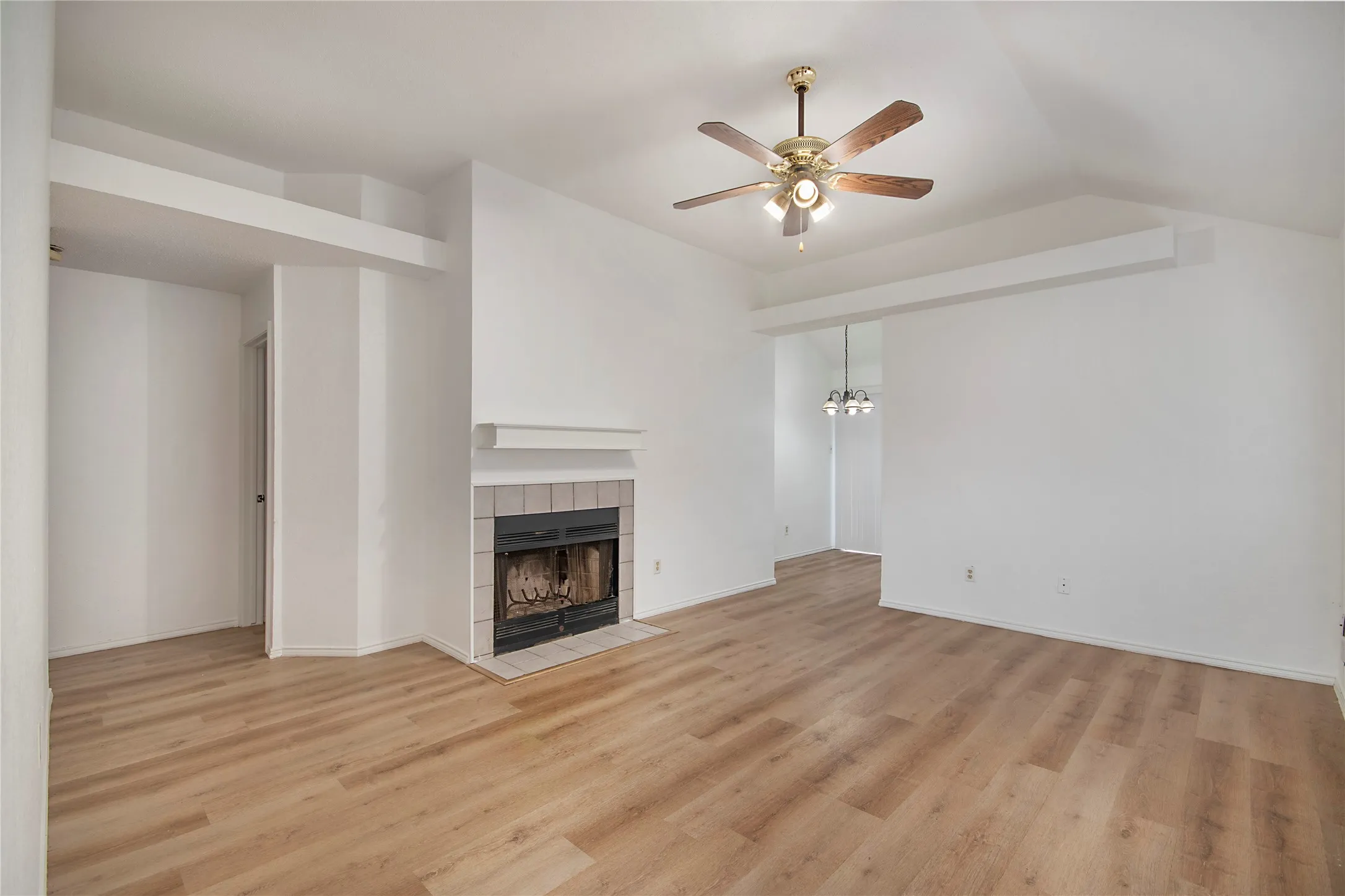 Varnished wood-finish flooring, vaulted ceiling, and a ceiling fan with integrated lighting