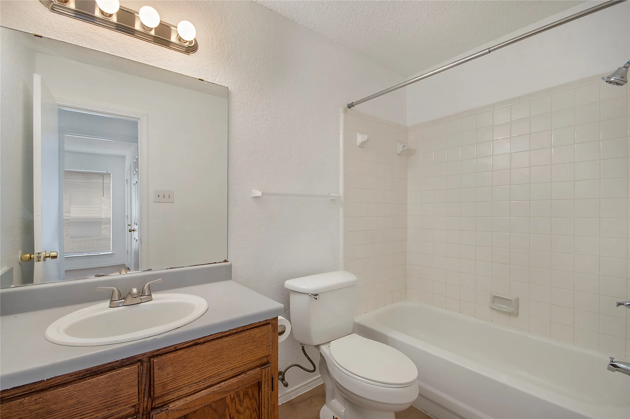 Wood-finish vanity with an integrated sink, broad mirror, and a three-light vanity bar
