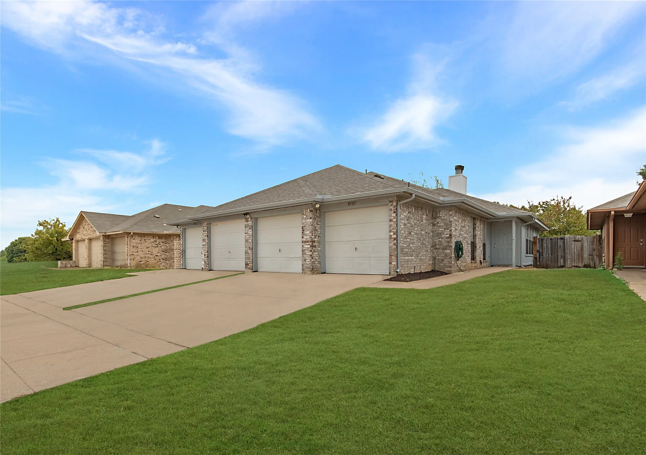 Brick exterior with multiple garage doors, concrete driveway, and a well-maintained lawn