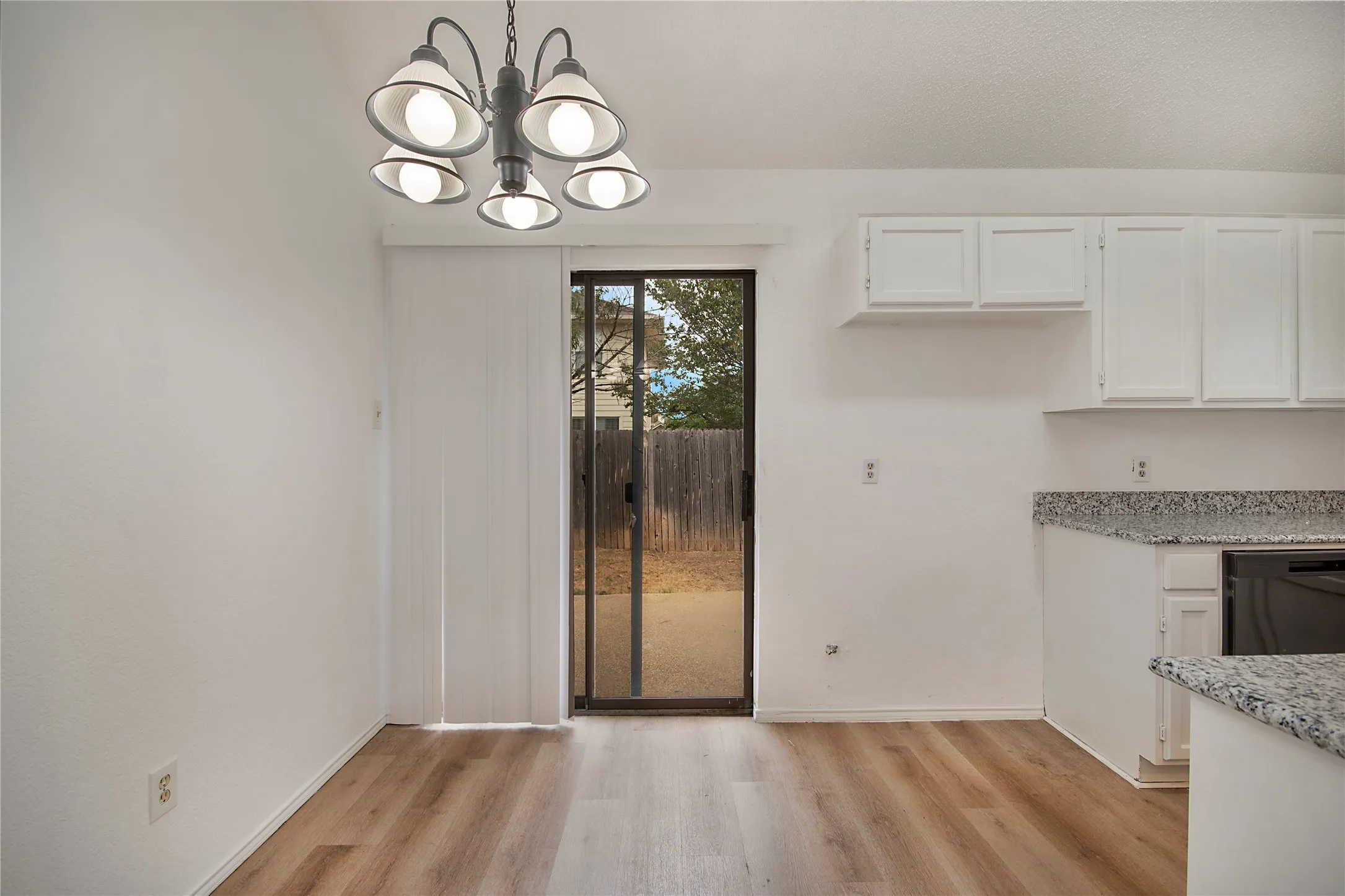 Wood-finish flooring, sliding glass door, overhead lighting fixture, white cabinetry, and granite-style countertops