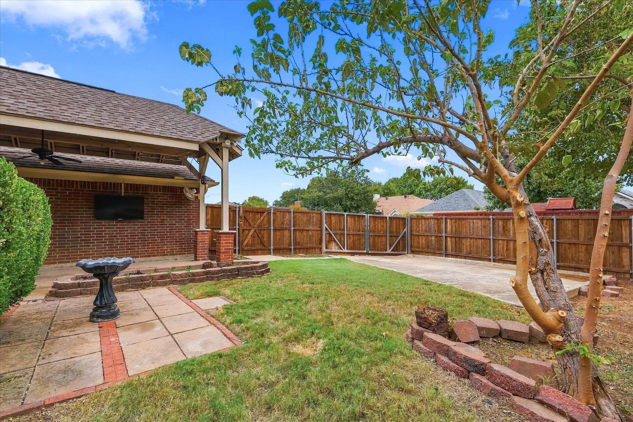 Expansive backyard featuring a wood privacy fence, a concrete patio, and a covered outdoor living area with a ceiling fan