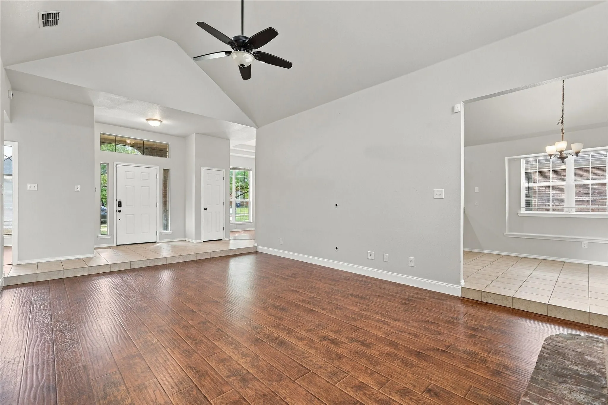 The unique step-down living room is designed to be the gathering space of the home, featuring vaulted ceilings, warm laminate flooring, recessed lighting, ceiling fan and a dramatic floor-to-ceiling brick gas fireplace with raised hearth and wood mantel, beautifully framed by windows.