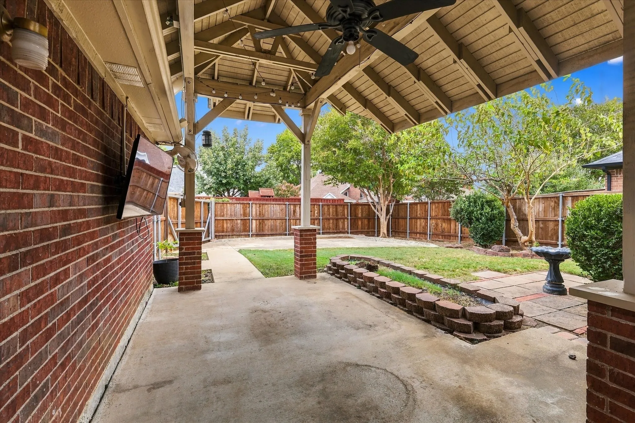 Covered patio featuring a ceiling fan, brick columns, concrete flooring, and a brick planter