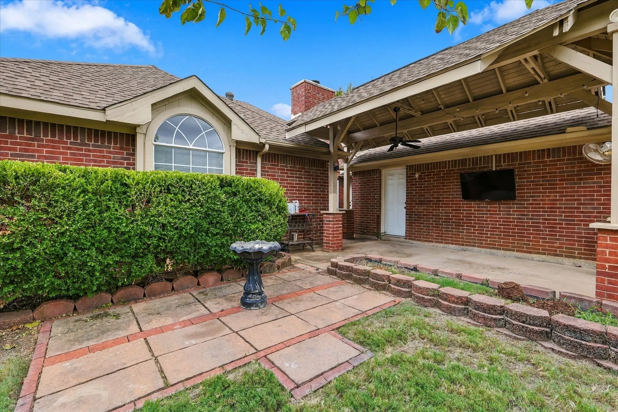 Brick exterior featuring an arched window, covered patio with a ceiling fan, and a paved walkway