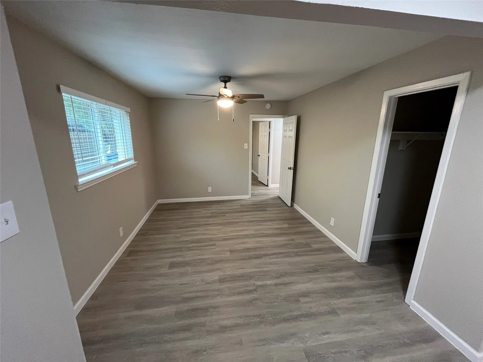 Neutral wall paint, wood-finish flooring, ceiling fan with light fixture, window with blinds, and built-in closet shelving