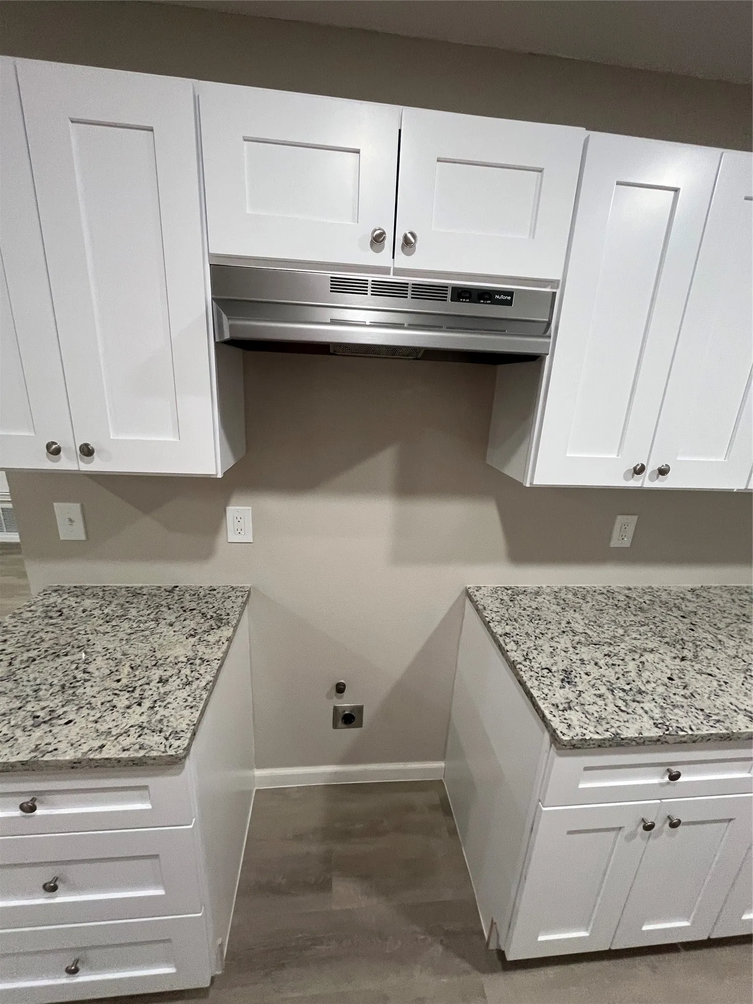 White shaker-style cabinetry, stainless steel range hood, light-toned wood-finish flooring, and granite countertops