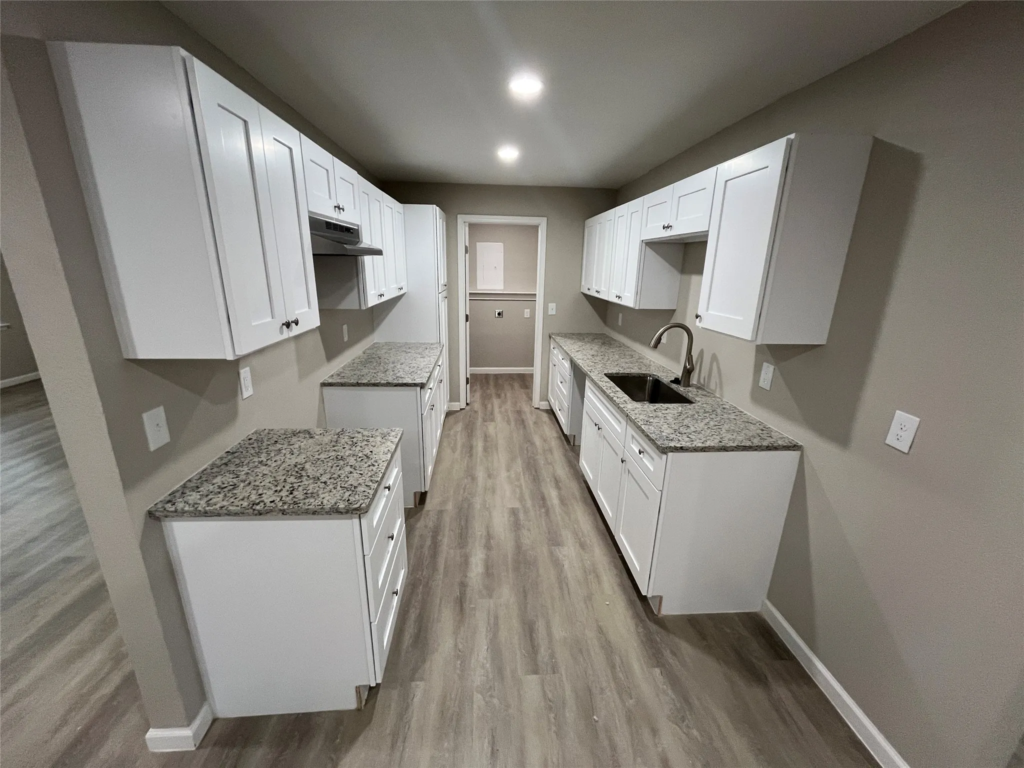 Contemporary galley kitchen featuring white shaker-style cabinetry, granite-style countertops, a double basin sink with a high-arch faucet, and wood-finish flooring