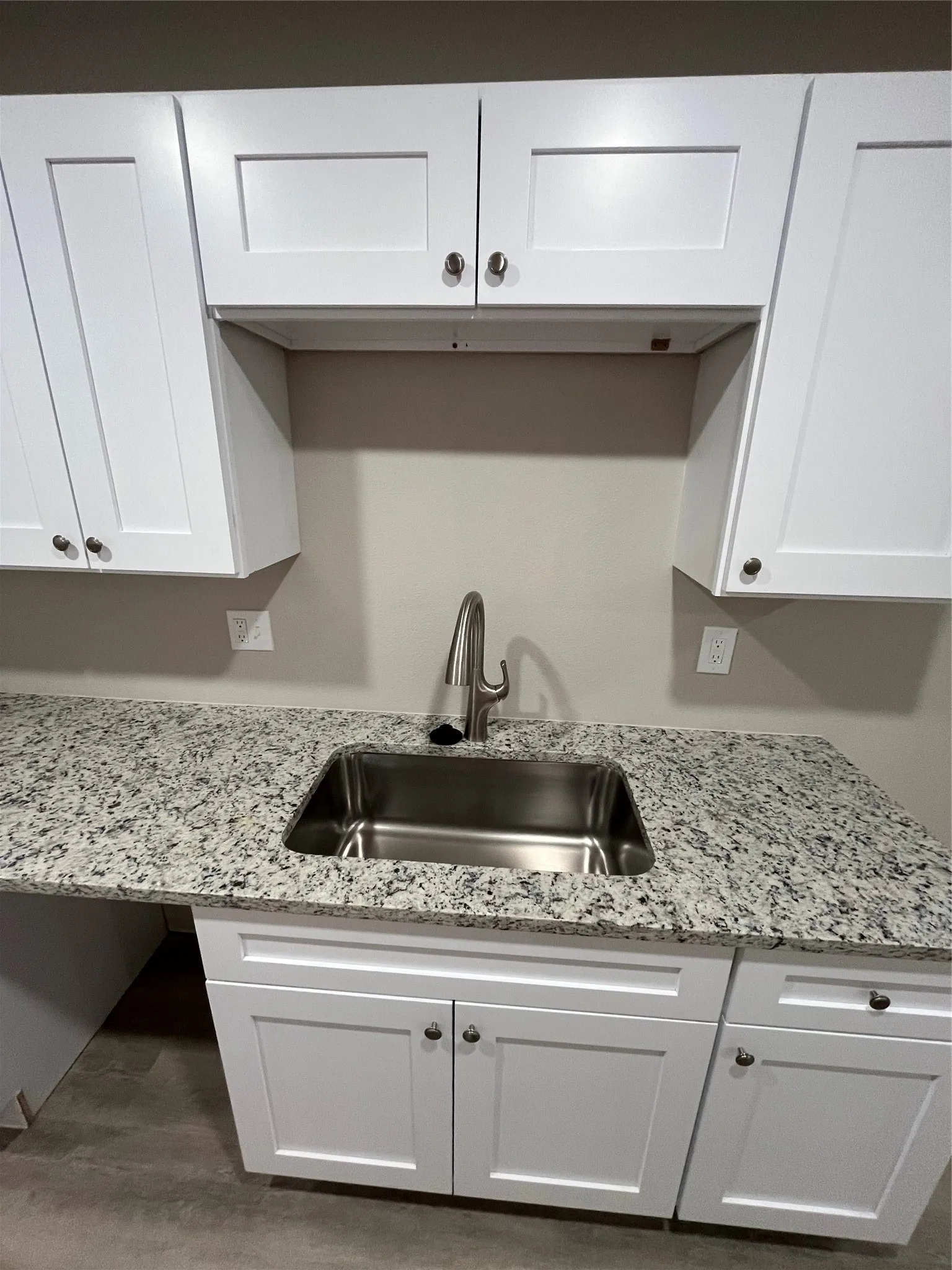 Stainless steel sink, granite-style countertop, white shaker cabinetry, and brushed nickel hardware