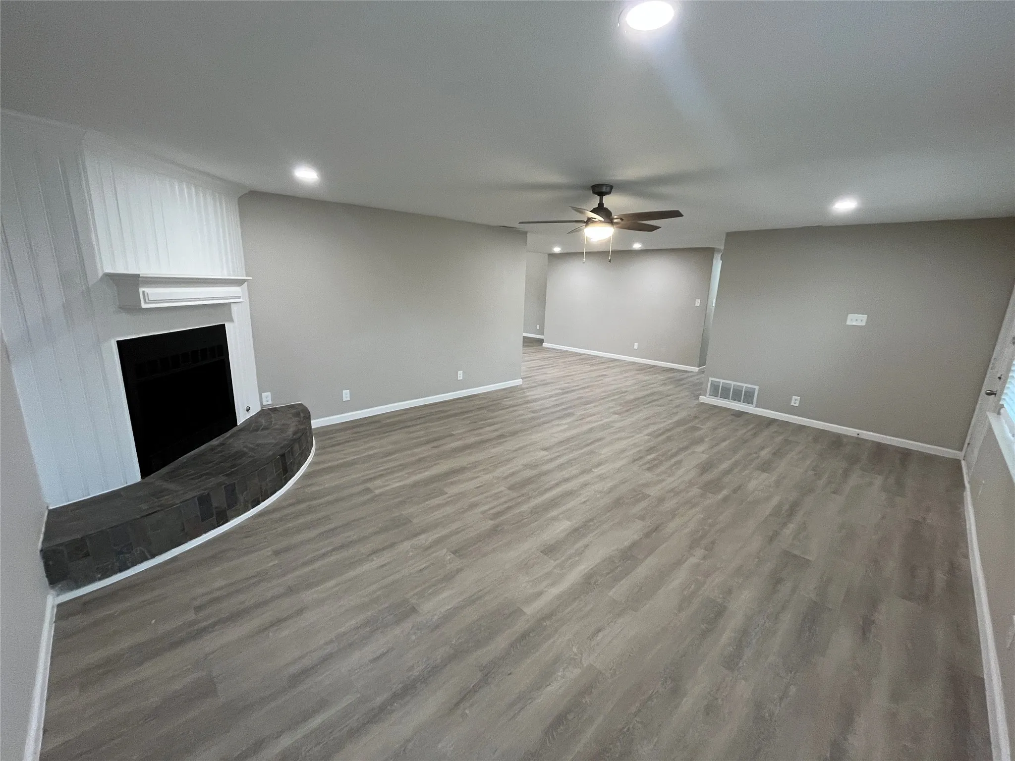 Spacious living area featuring wood-finish flooring, a fireplace with a stone hearth, and recessed lighting