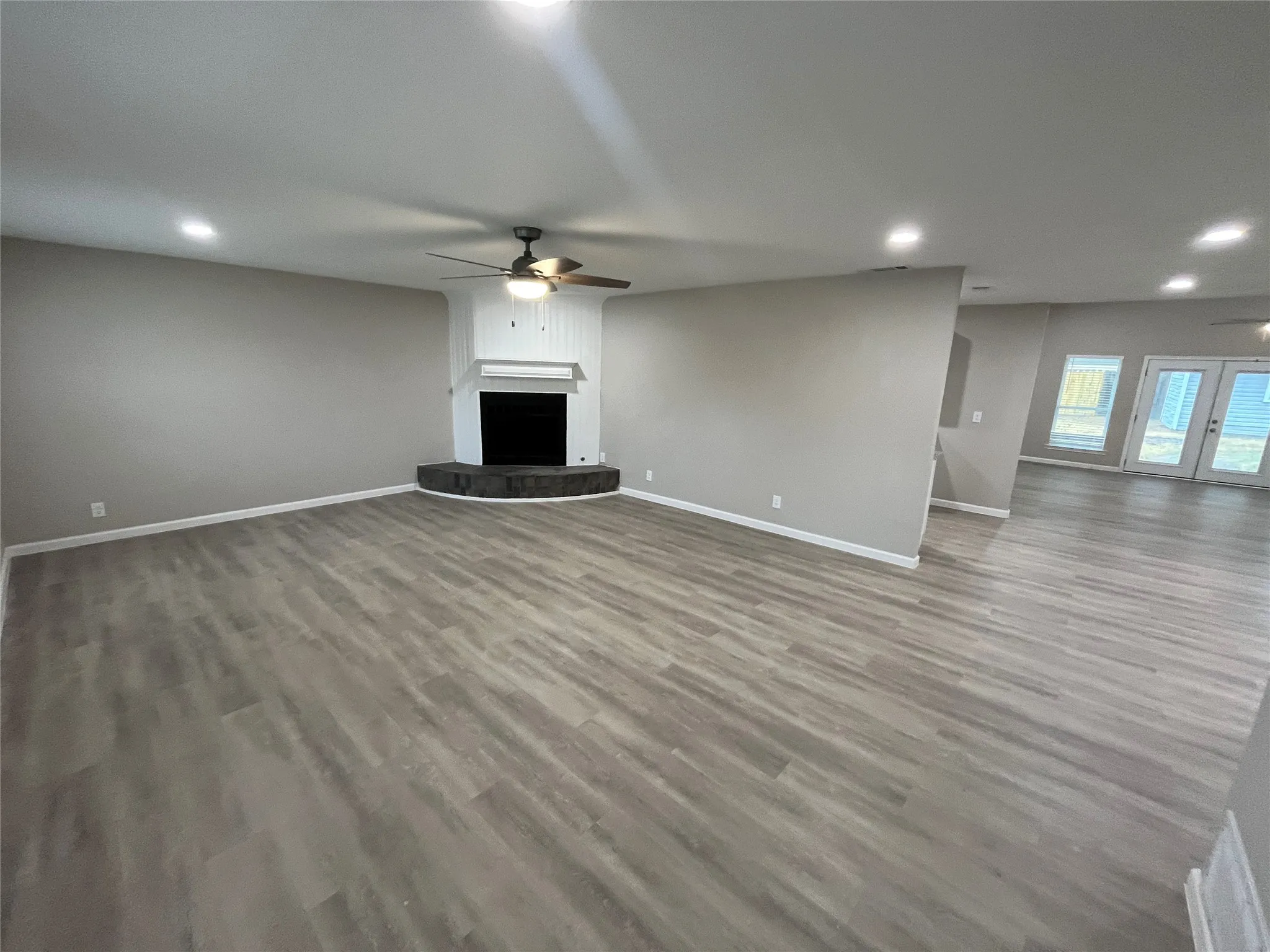 Spacious living area featuring wood-finish flooring, recessed lighting, and a corner fireplace with a dark stone hearth