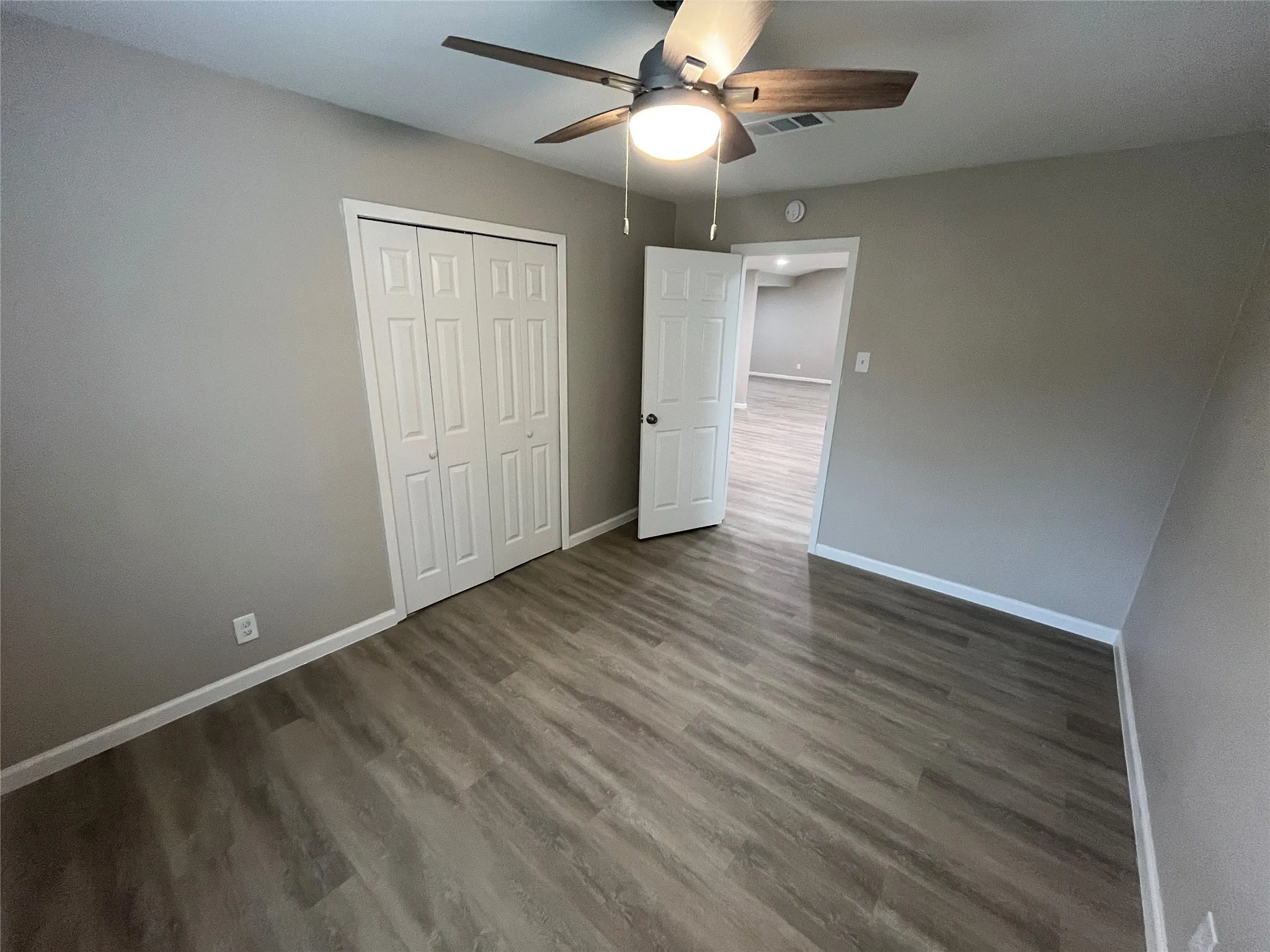 Light gray wall color, wood-finish flooring, white trim, ceiling fan with integrated lighting, and a white bi-fold closet door