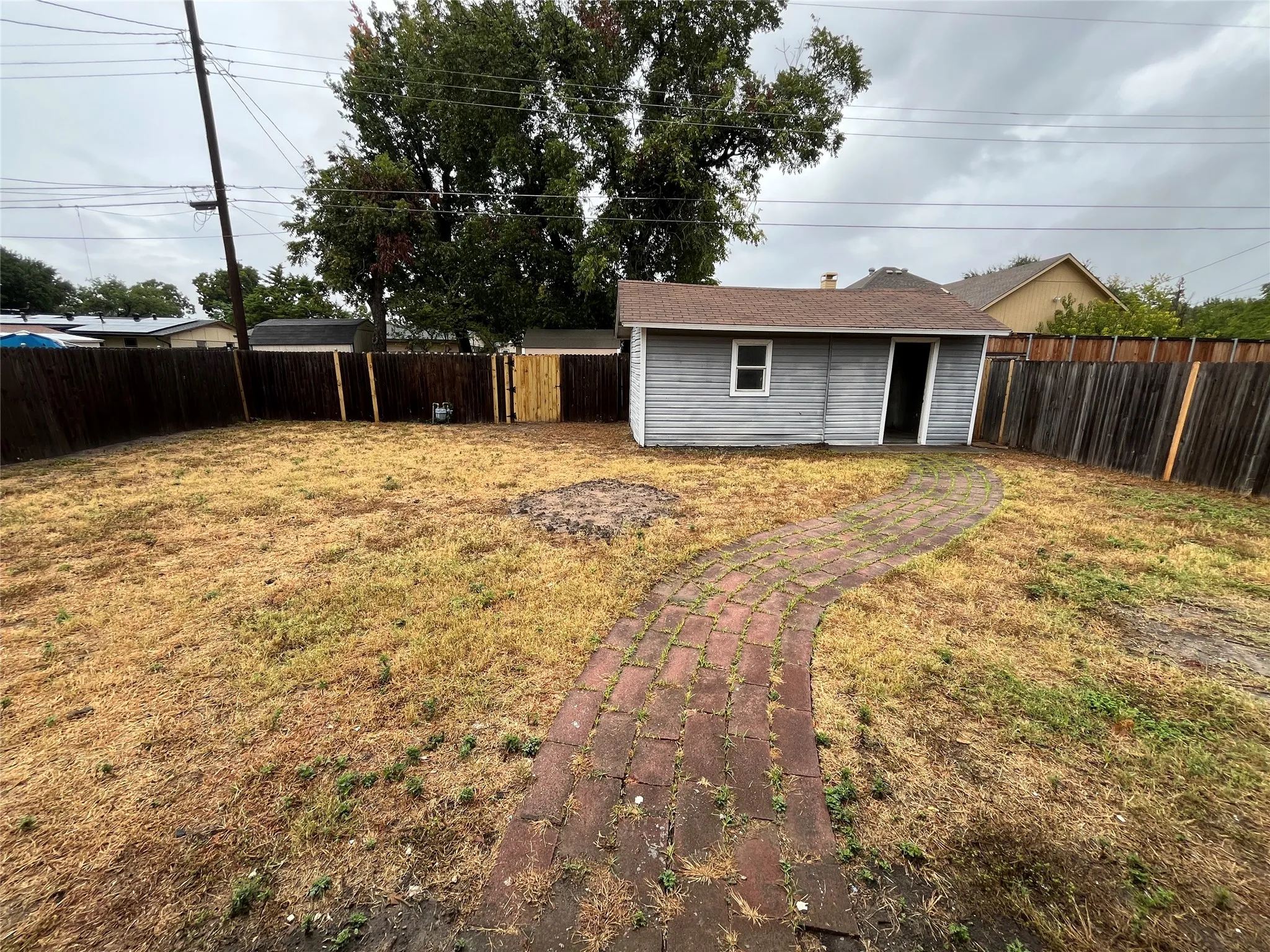 Fenced backyard featuring a brick pathway and a detached storage shed