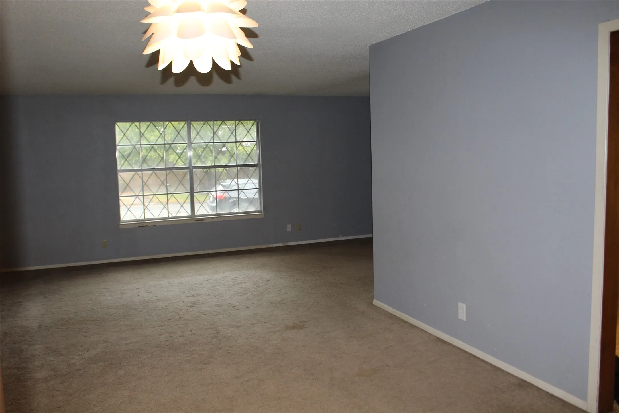 Spacious room featuring carpet flooring, a window with security bars, and a decorative ceiling light fixture