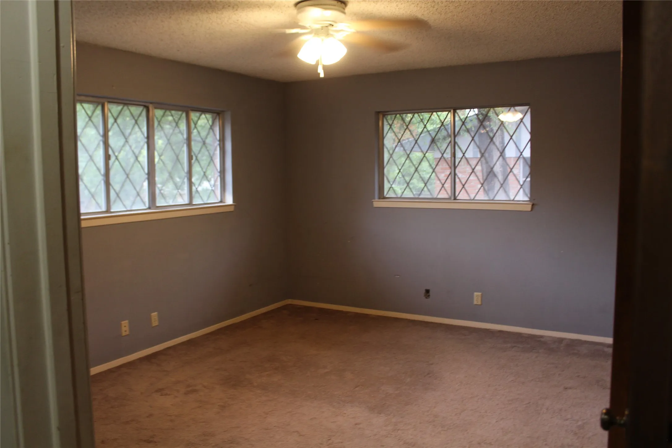 Carpeted flooring, two windows, ceiling fan with light, and light gray wall paint