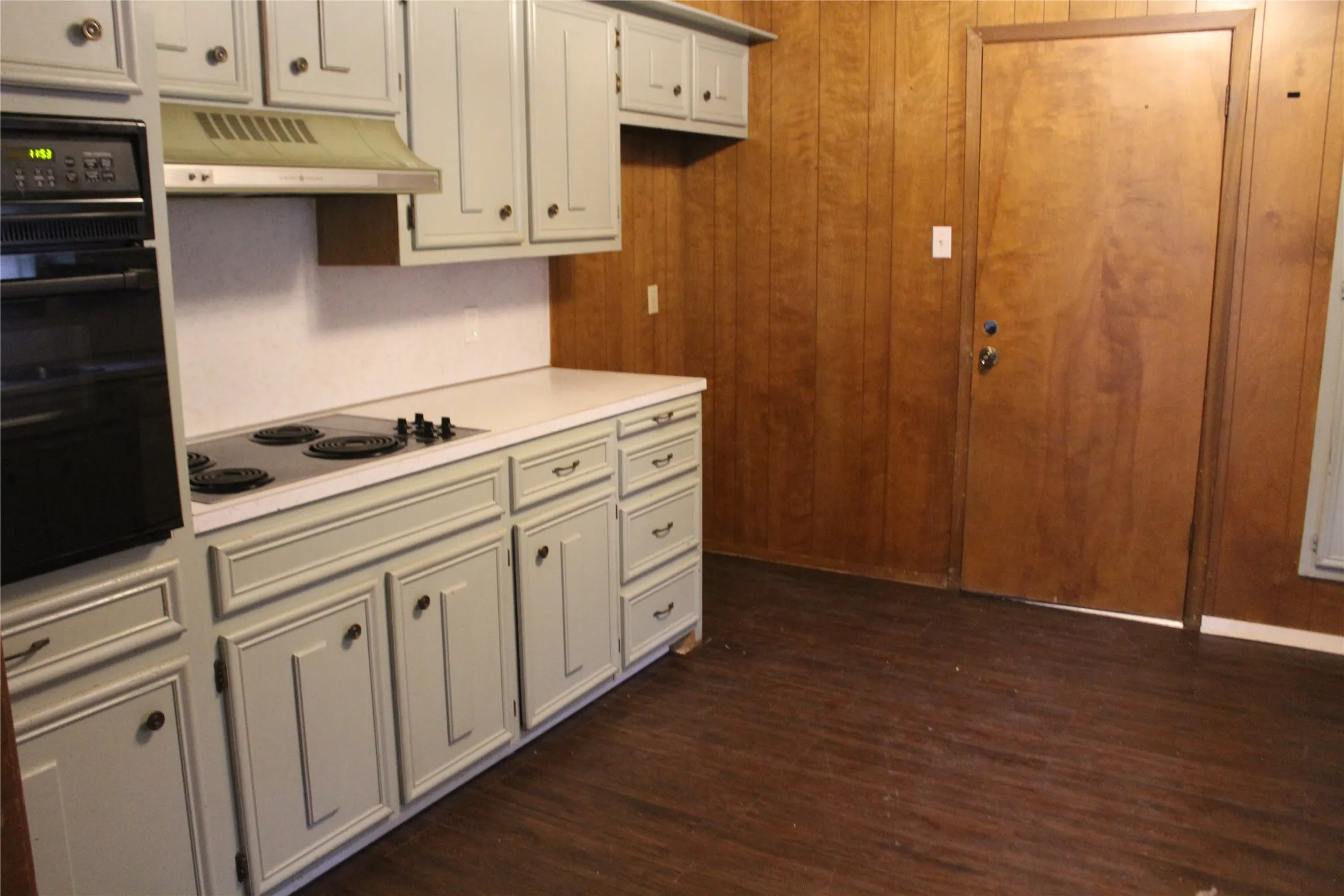 Kitchen featuring painted cabinetry, an integrated oven, a built-in stovetop, an extractor hood, and wood-finish flooring