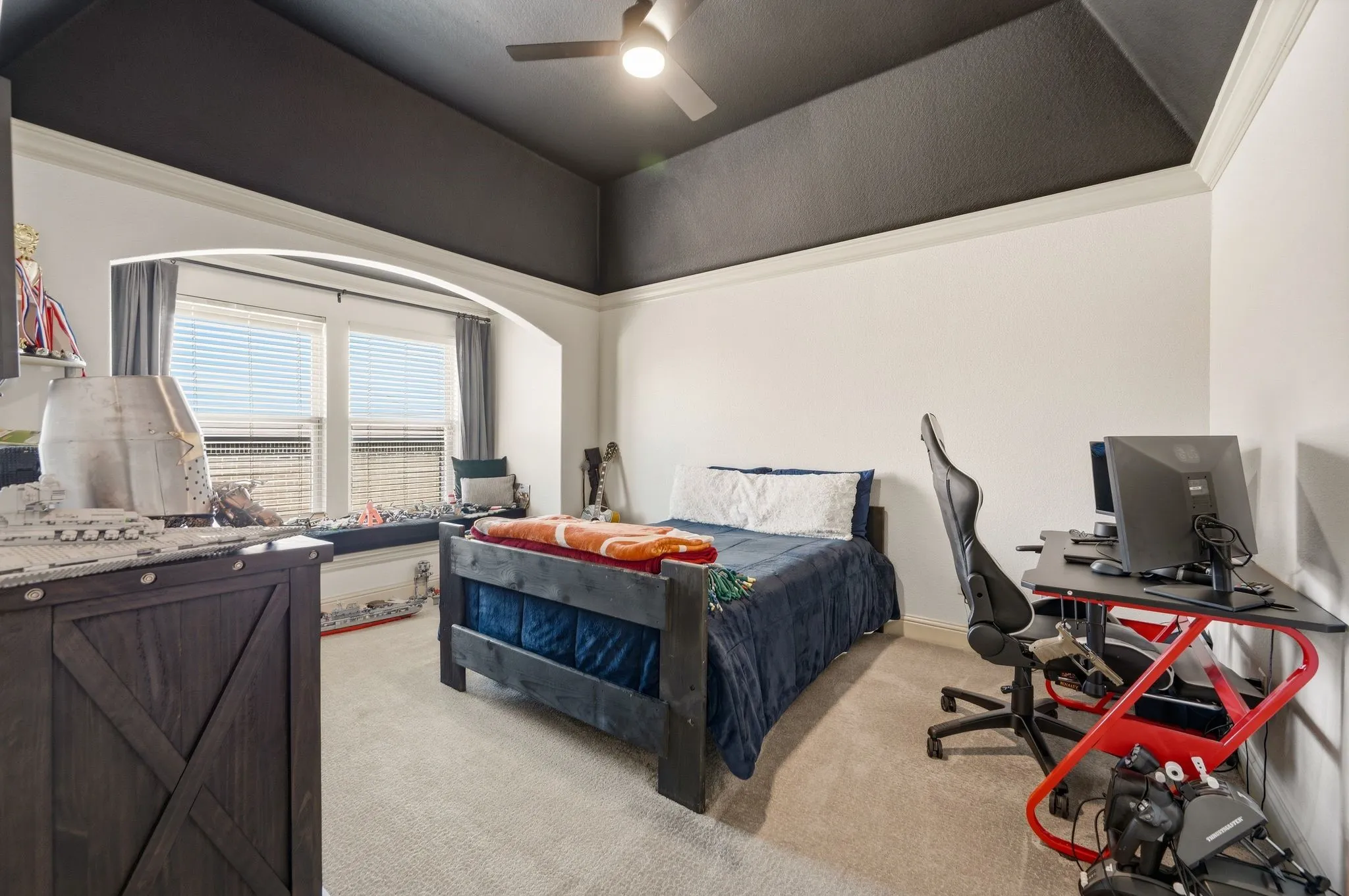 Tray ceiling with crown molding, ceiling fan, arched window alcove, window seat, and built-in window blinds