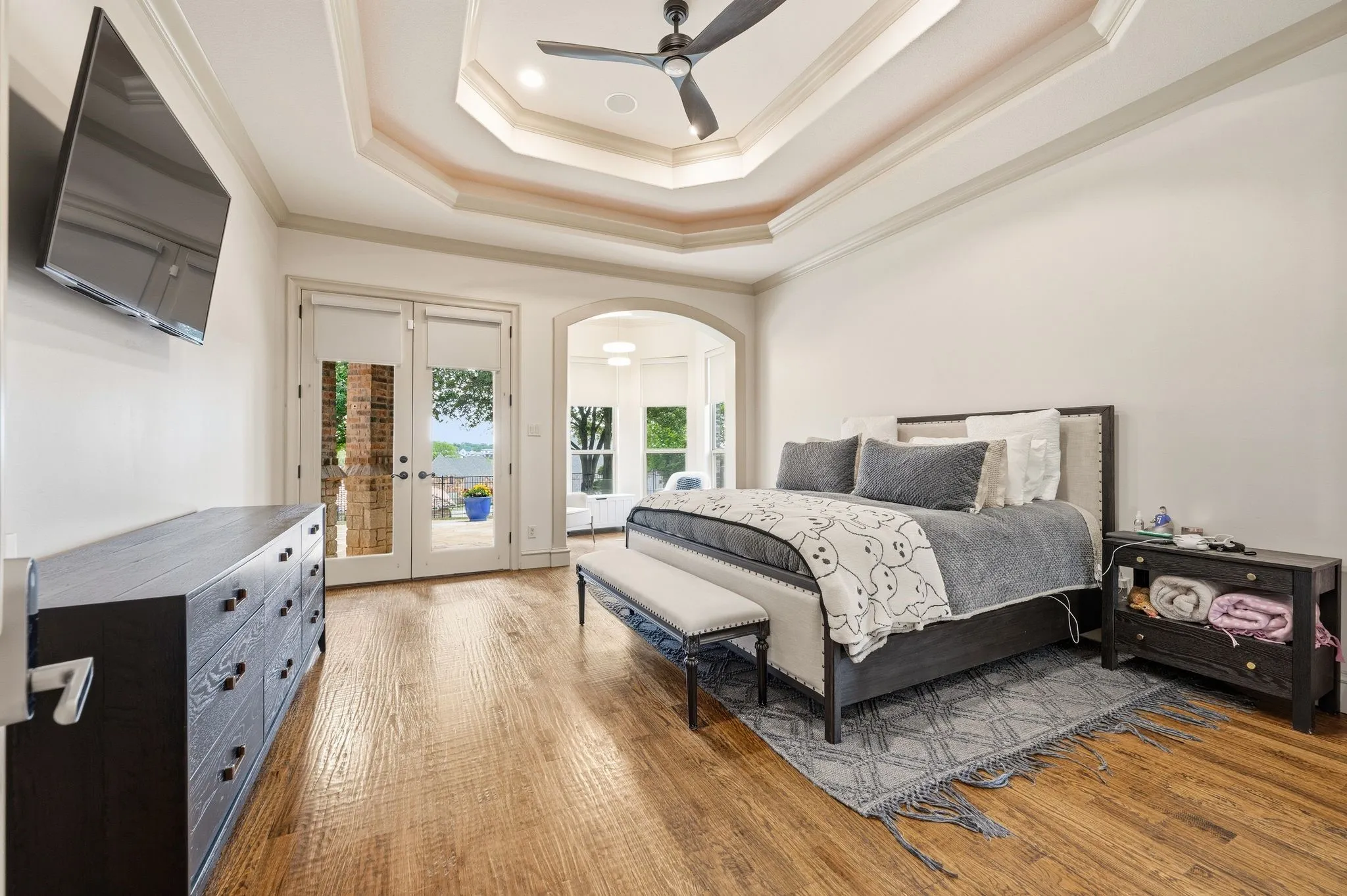 Tray ceiling with recessed lighting and ceiling fan, wood-finish flooring, and double glass-paneled doors leading to an outdoor space