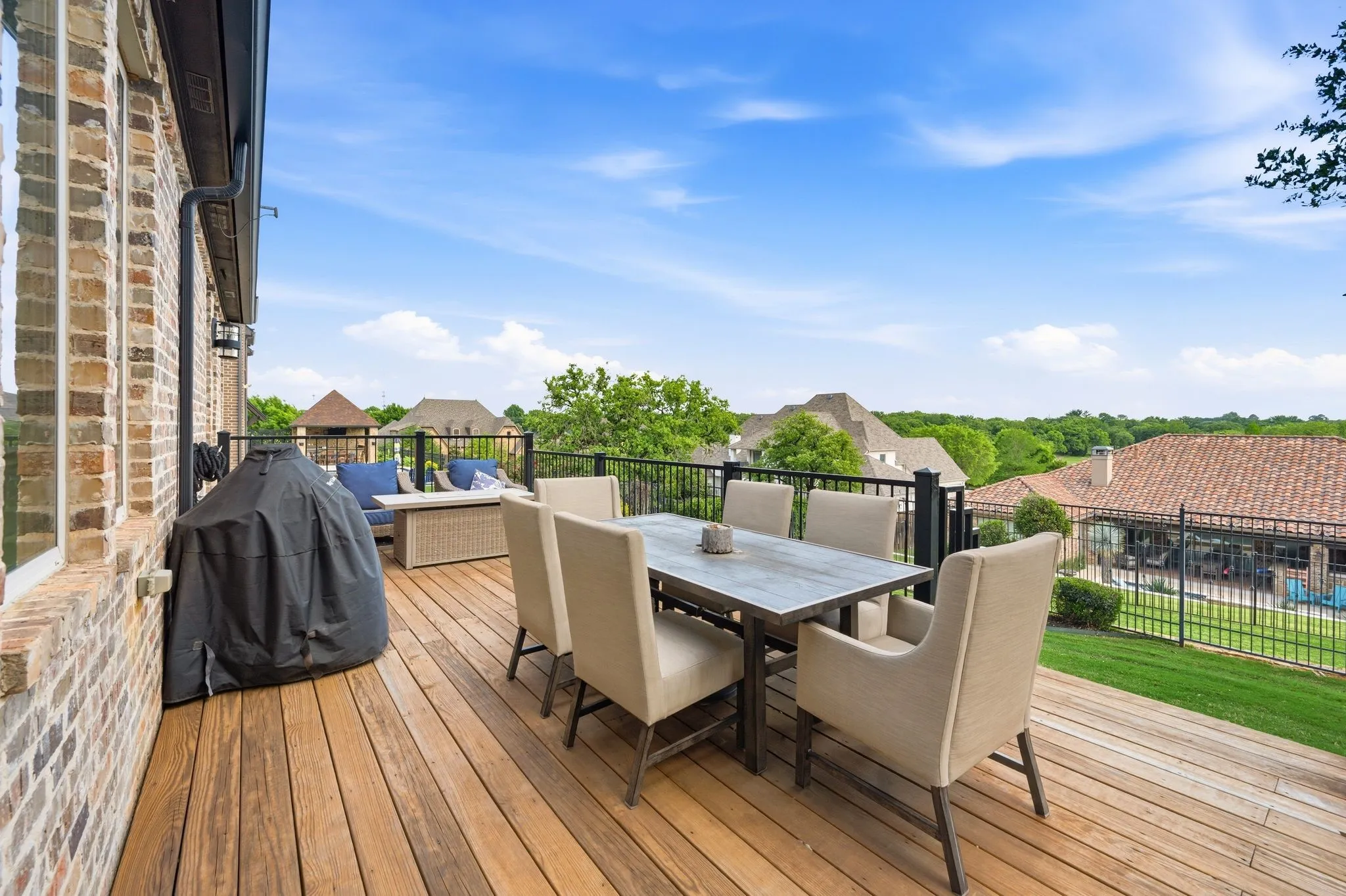 Expansive wood deck with black metal railing, featuring a brick exterior wall and a green lawn