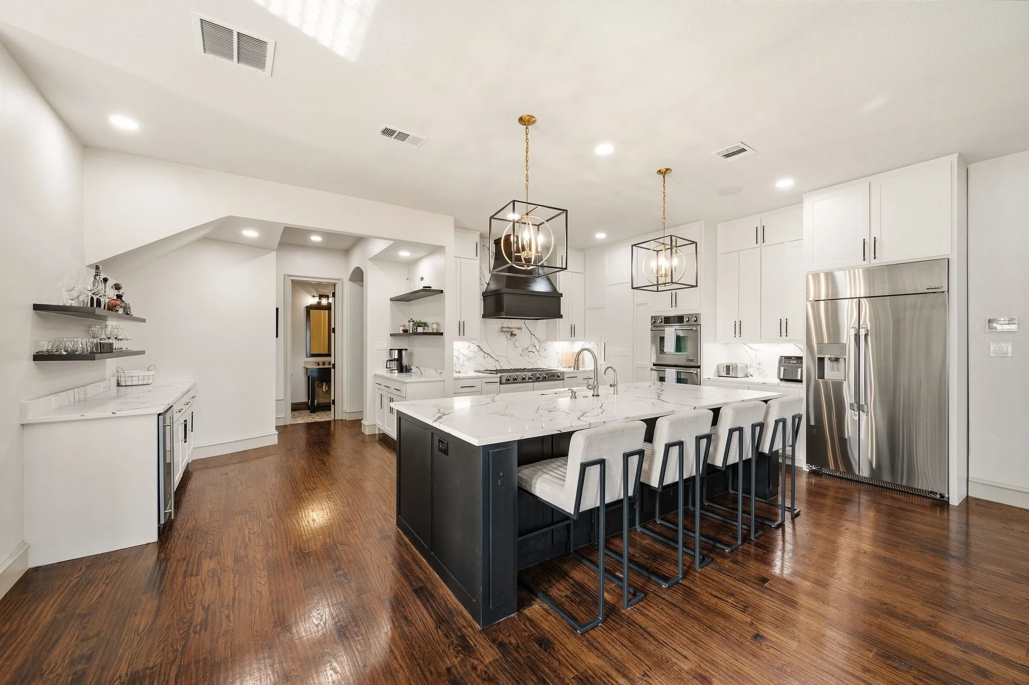 Expansive kitchen featuring wood-finish flooring, white cabinetry, a large center island with seating, and stainless steel appliances