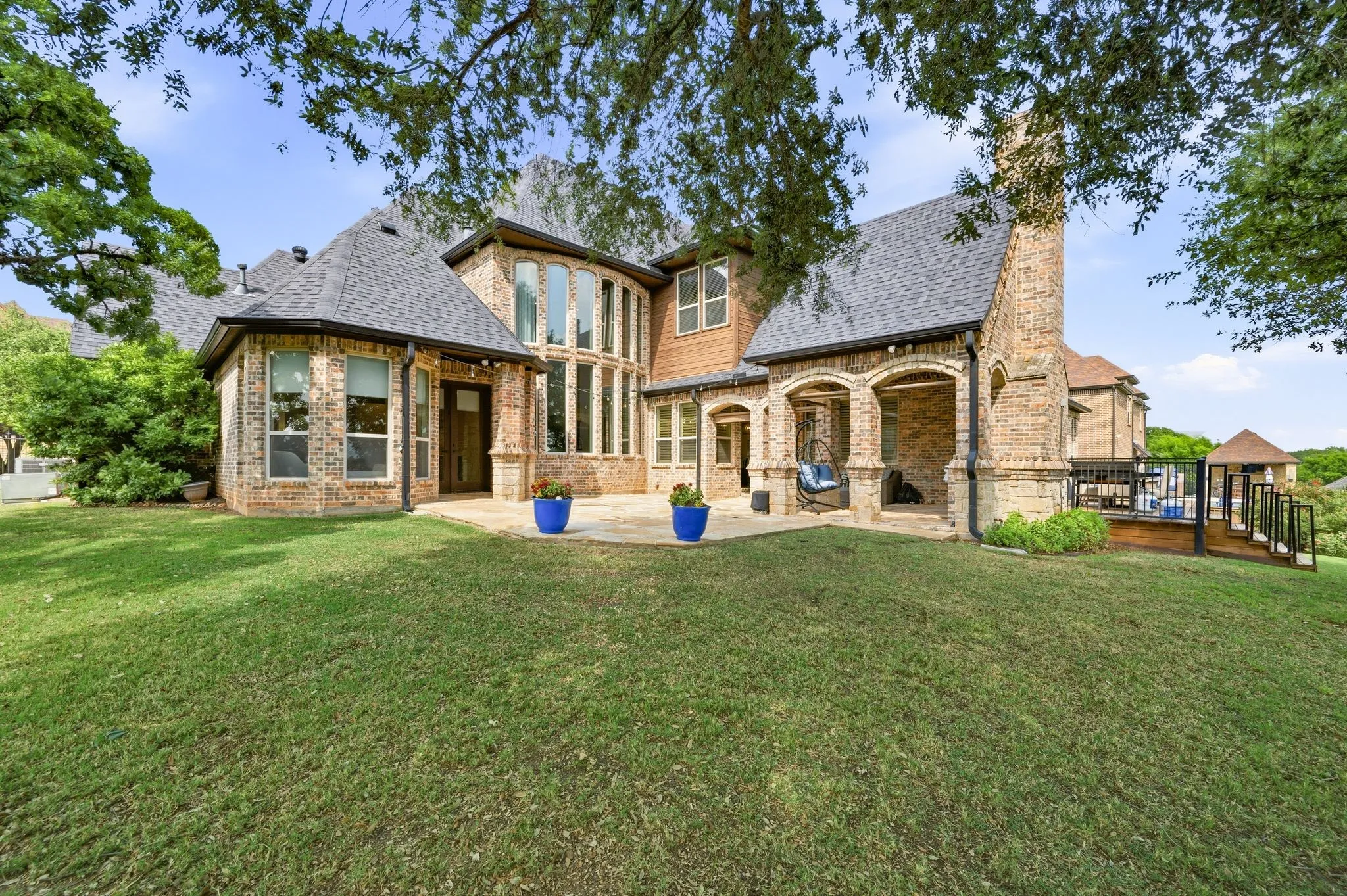 Brick exterior with arched covered patio, expansive multi-pane windows, and a raised wood deck with steps