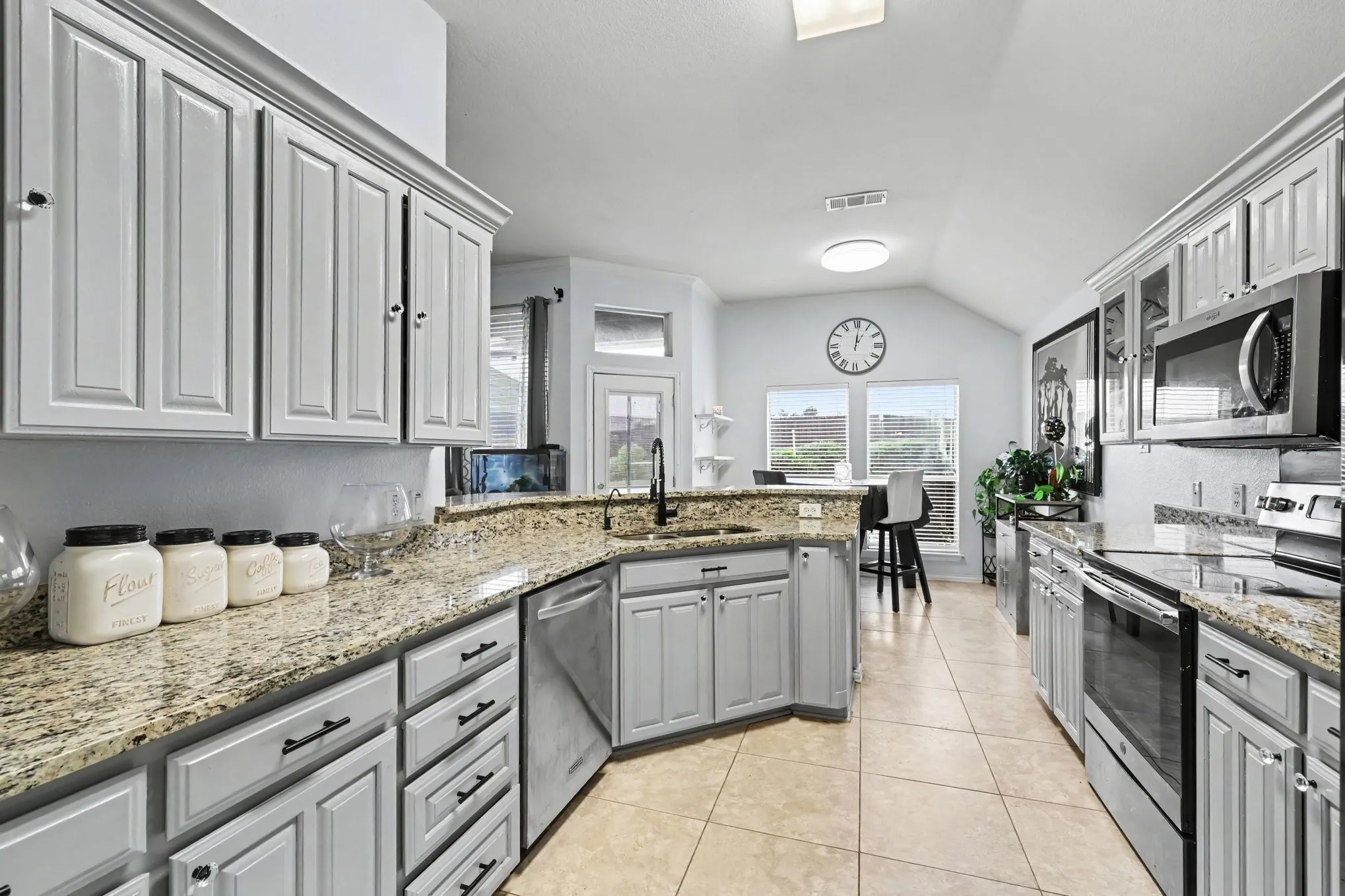 Kitchen featuring granite countertops, stainless steel appliances, white cabinetry, tile flooring, and a vaulted ceiling
