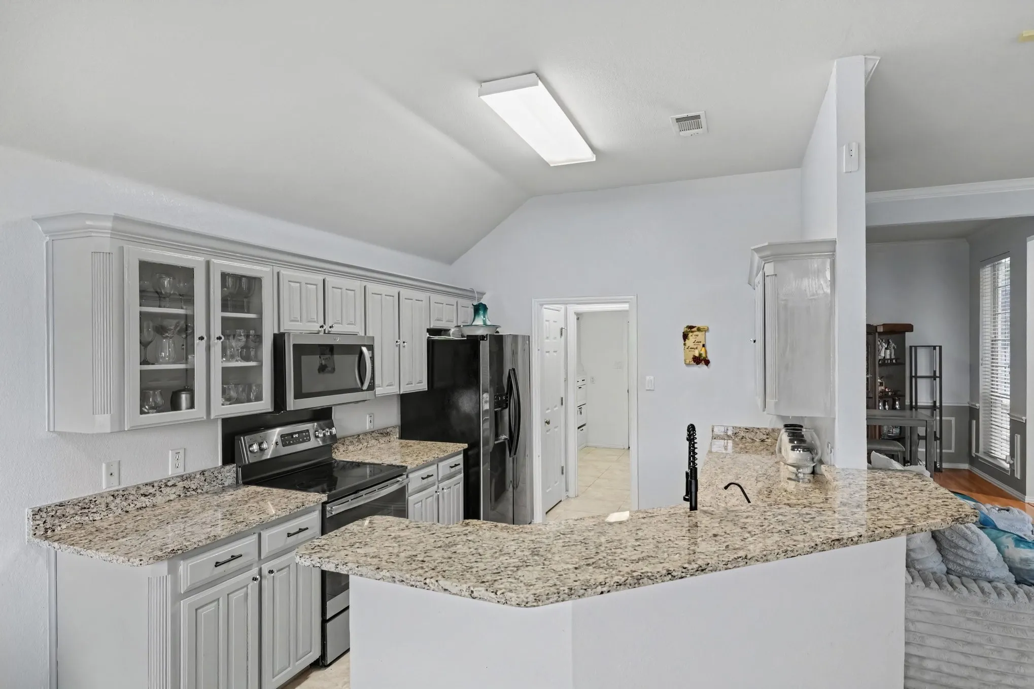 Kitchen featuring extensive light-toned cabinetry, granite countertops, stainless steel and black appliances, a high vaulted ceiling, and recessed lighting