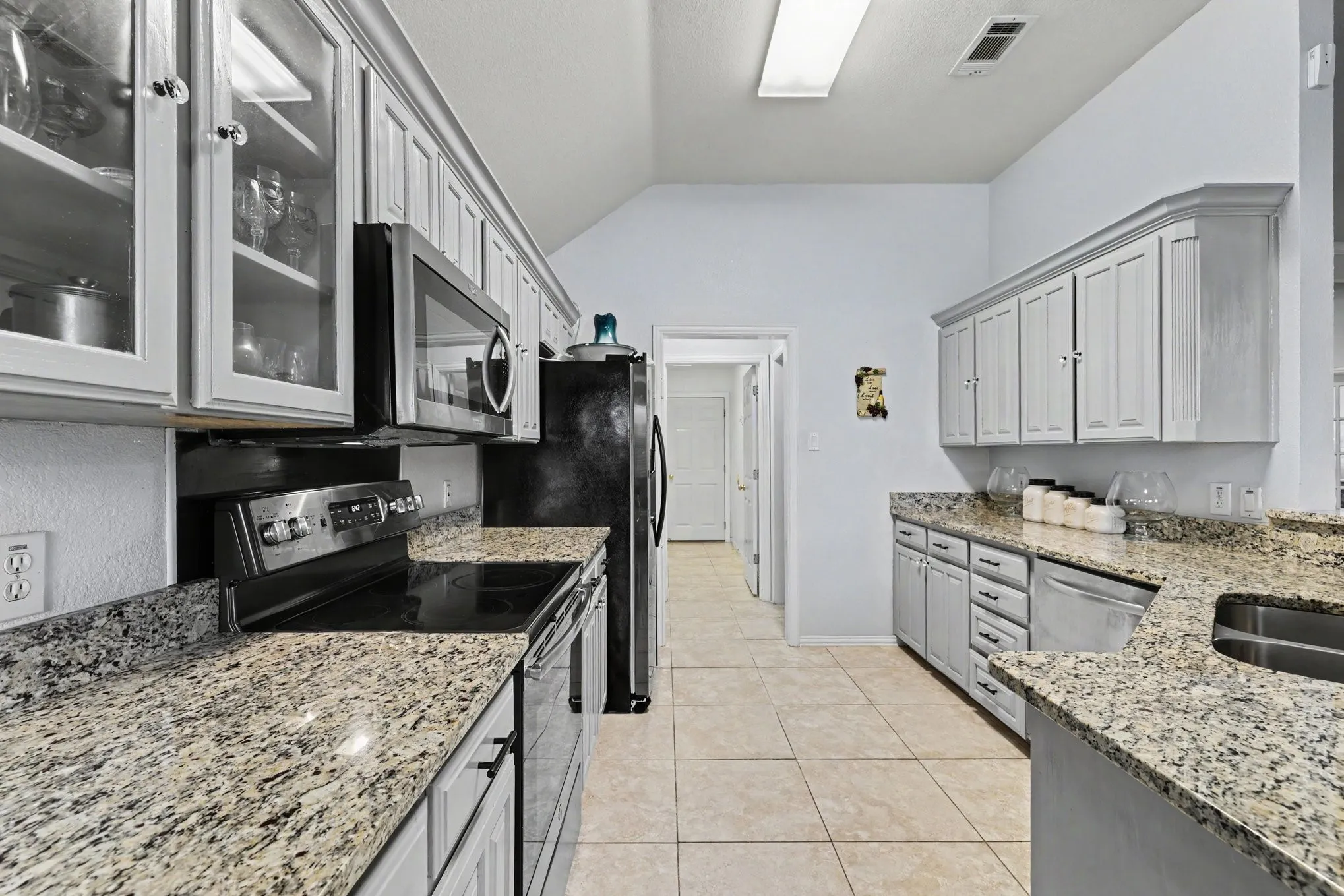 Kitchen featuring granite countertops, tile flooring, built-in microwave, and painted cabinetry with glass-front accents