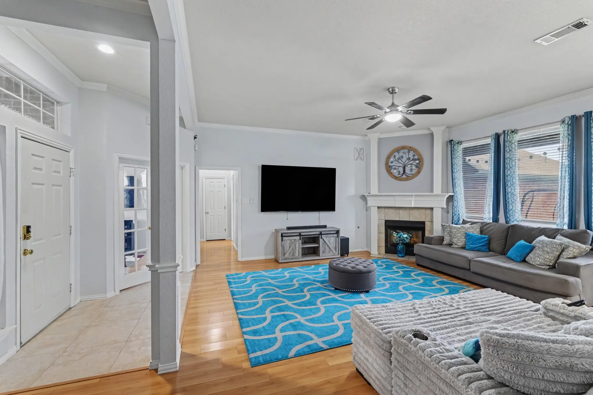 Expansive living area featuring wood-finish flooring, a corner fireplace with a mantel, and a ceiling fan