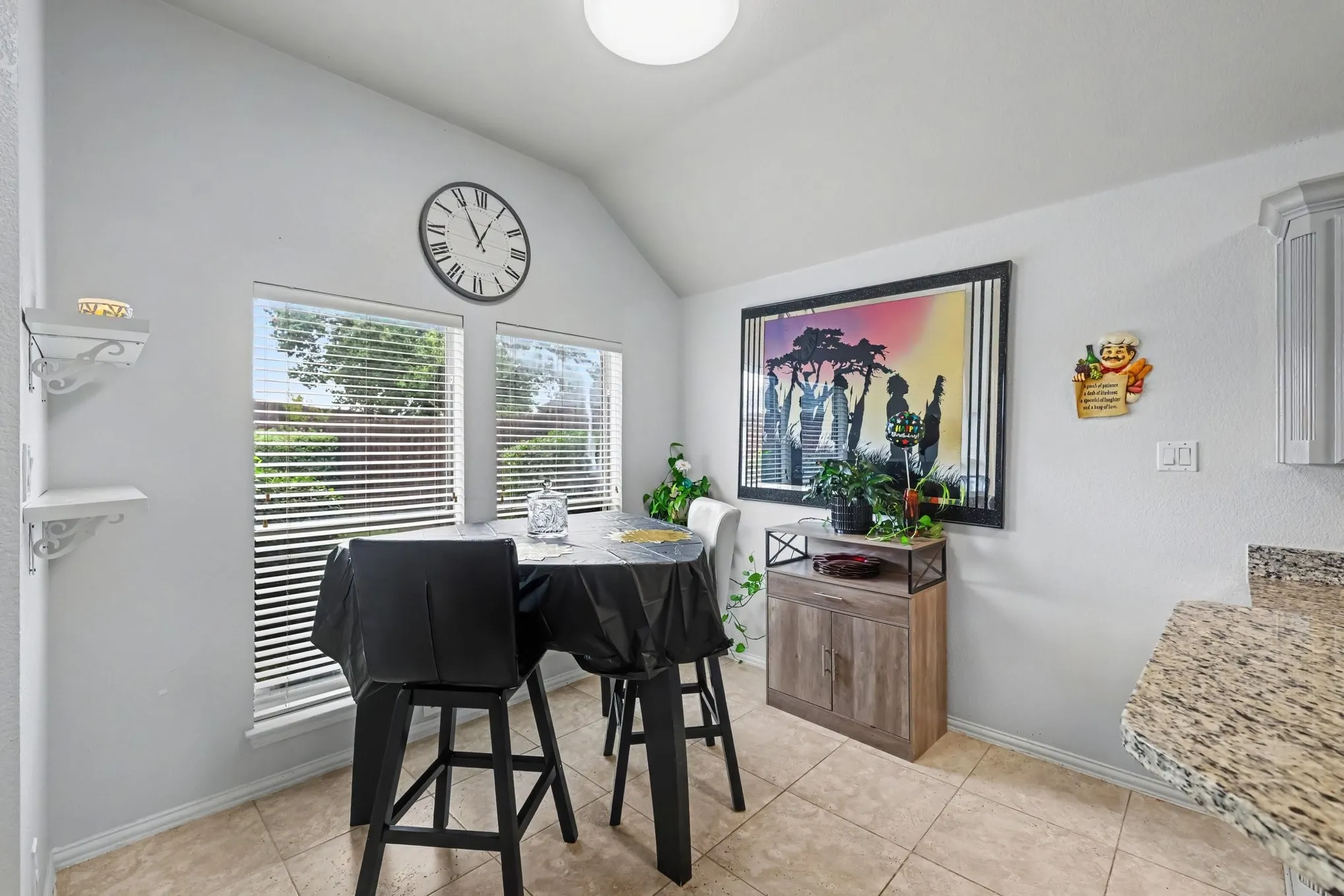 Vaulted ceiling, two windows with blinds, built-in shelving, tile flooring, and granite-look countertop