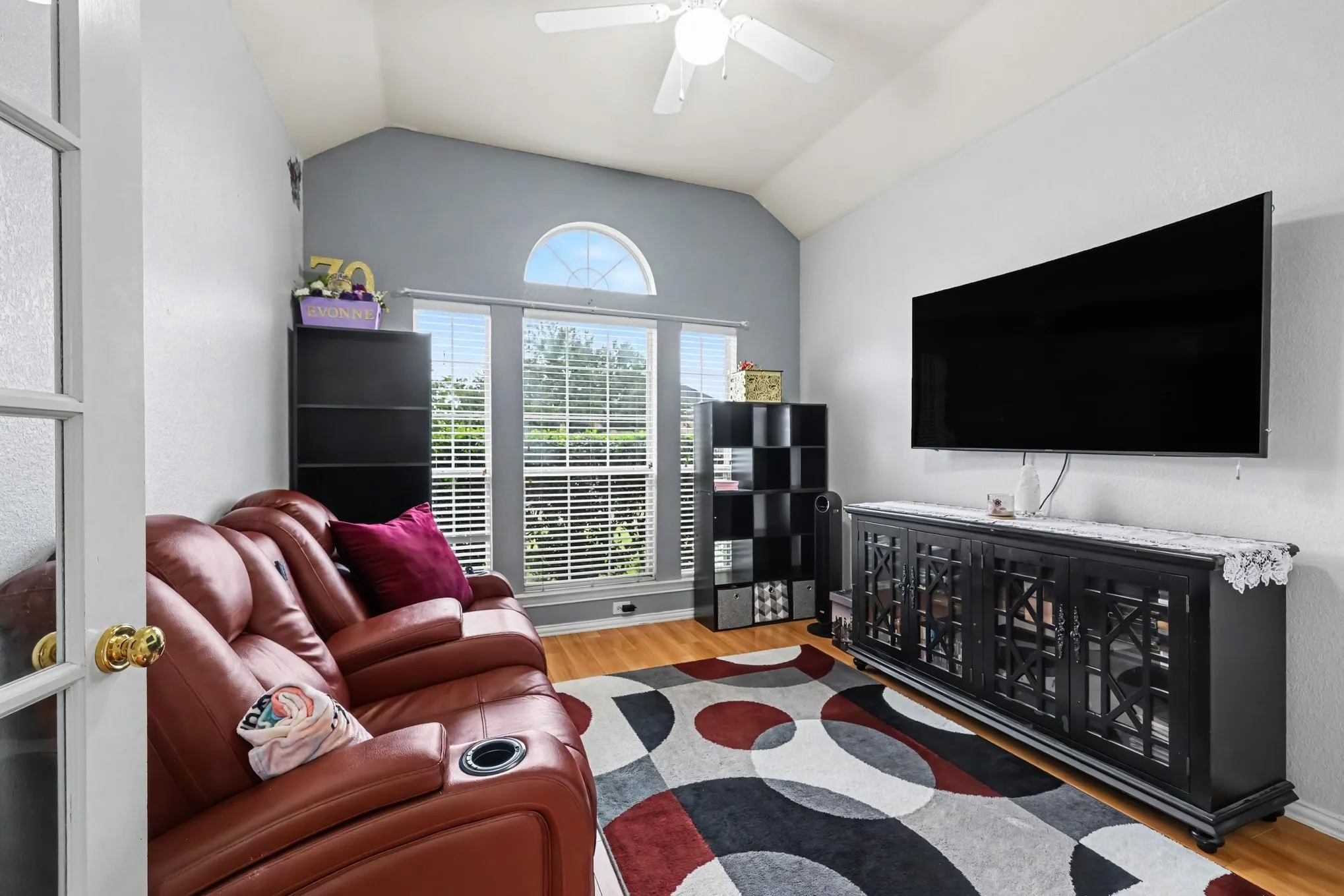 Vaulted ceiling with a ceiling fan, arched transom window, wood-finish flooring, and a built-in media console