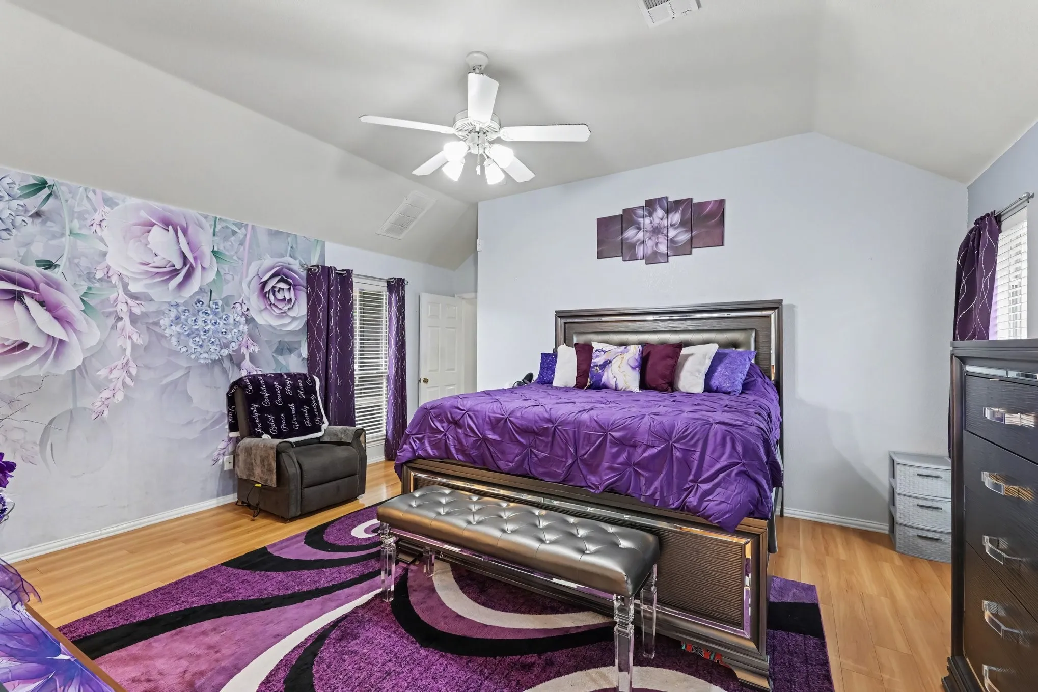 Vaulted ceiling with an attached ceiling fan, wood-finish flooring, and a decorative accent wall