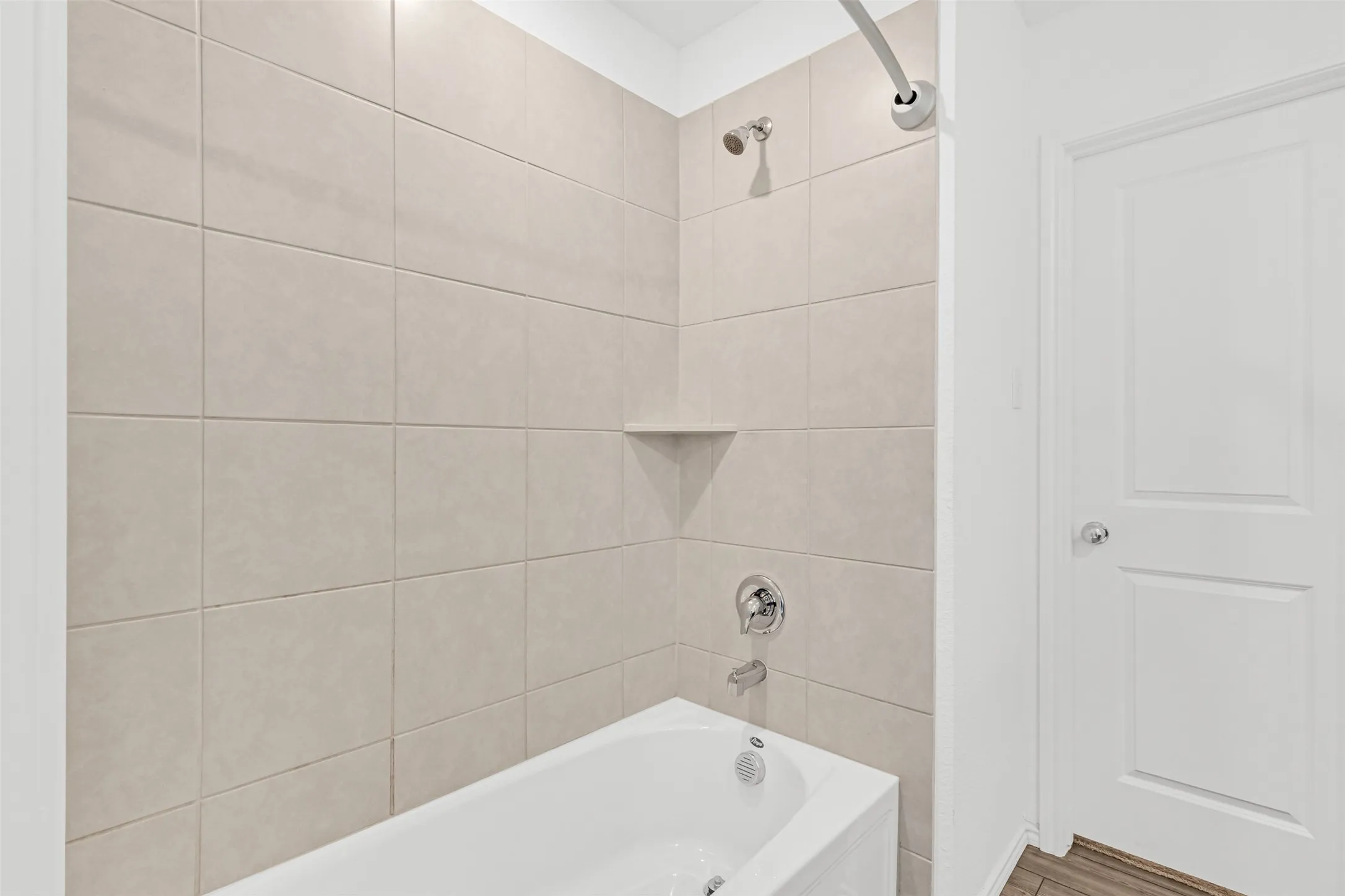 Bathtub with chrome fixtures, tiled shower surround, recessed shower shelf, and a shower head