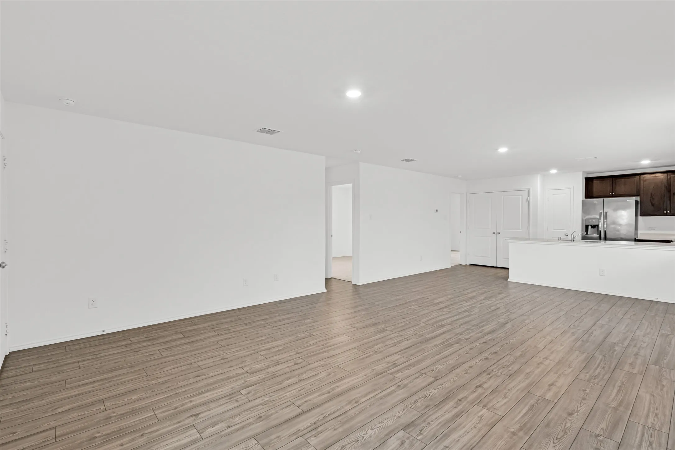 Spacious open-concept living area with wood-finish flooring throughout, recessed ceiling lighting, and seamless sightlines to the kitchen