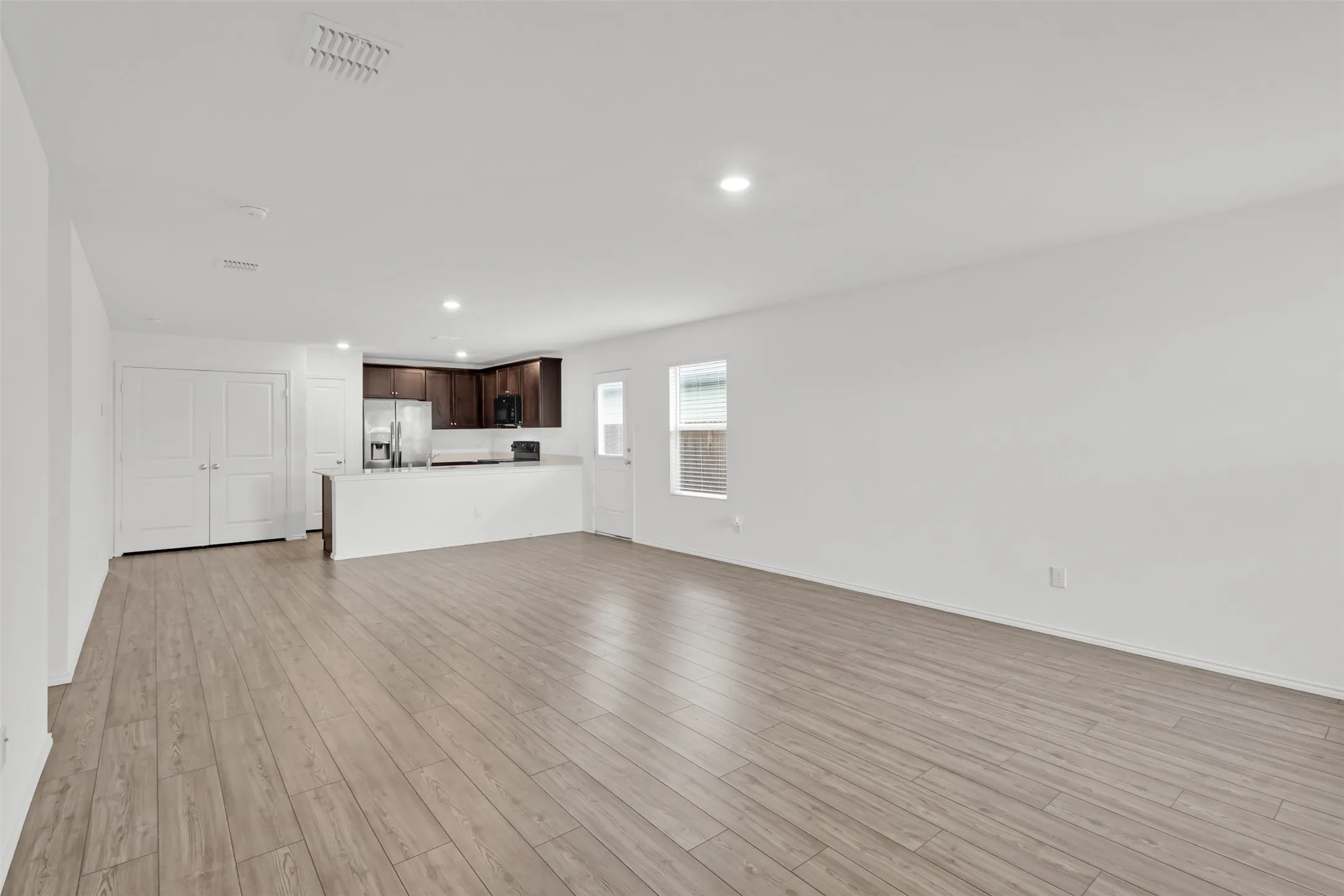 Open-concept living space featuring wood-finish flooring, recessed lighting, and a kitchen with dark wood cabinetry and a peninsula countertop