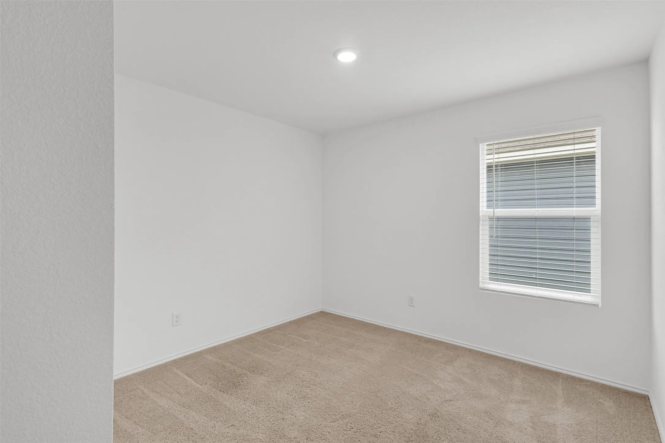 Recessed ceiling light, neutral-toned carpet, and a window with blinds