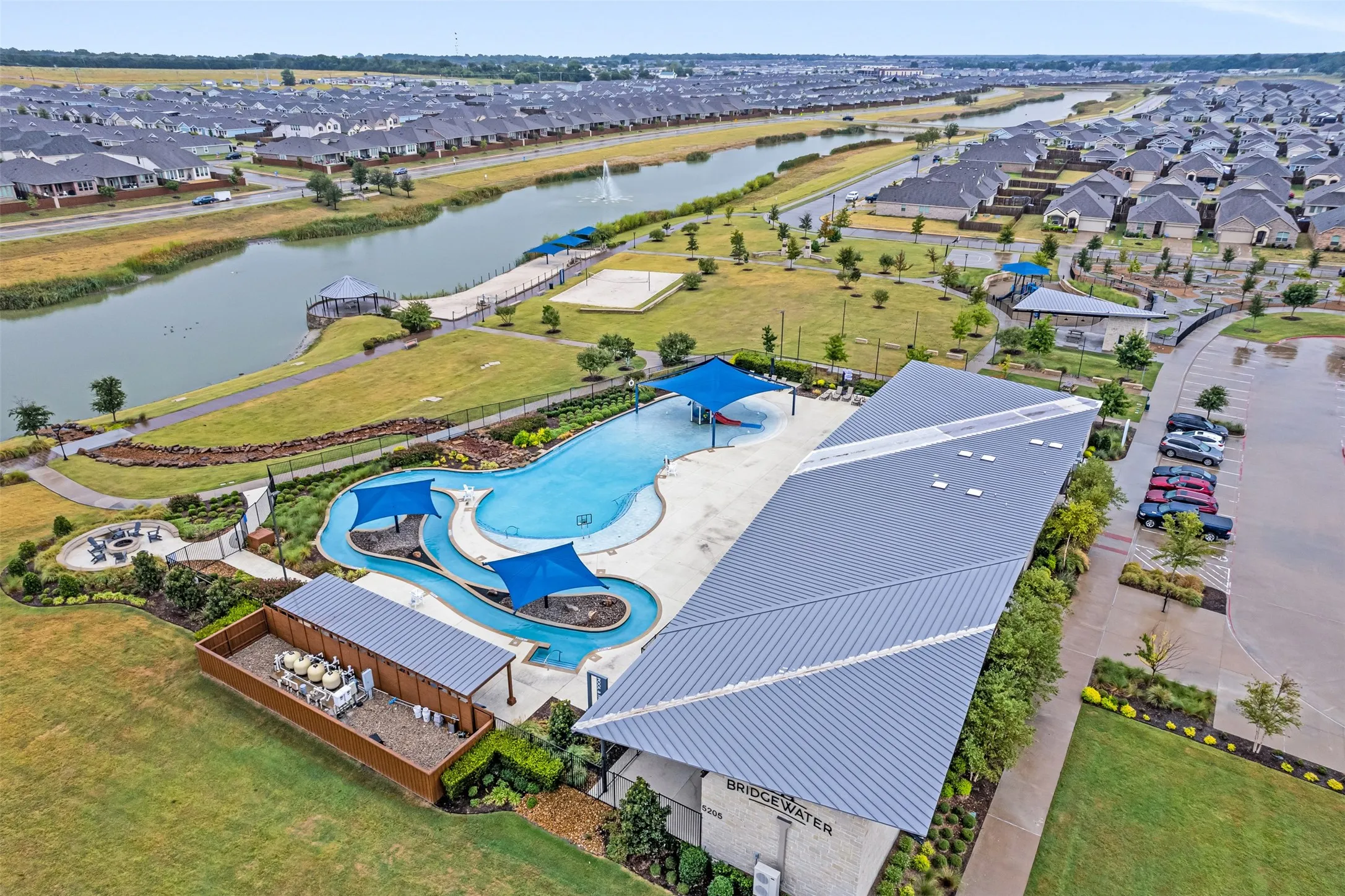 Community swimming pool with water slides, adjacent building with metal roof, and surrounding green spaces