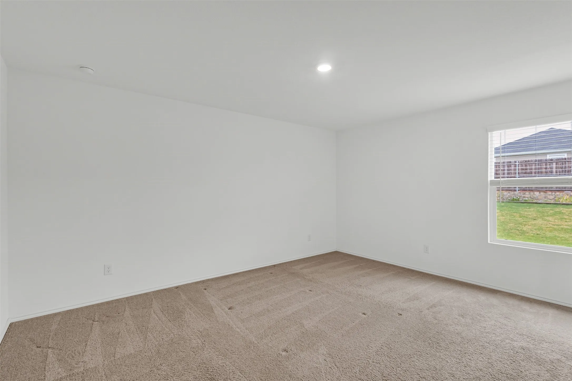 Recessed ceiling light, neutral wall paint, carpeted flooring, window with blinds, and exterior green space