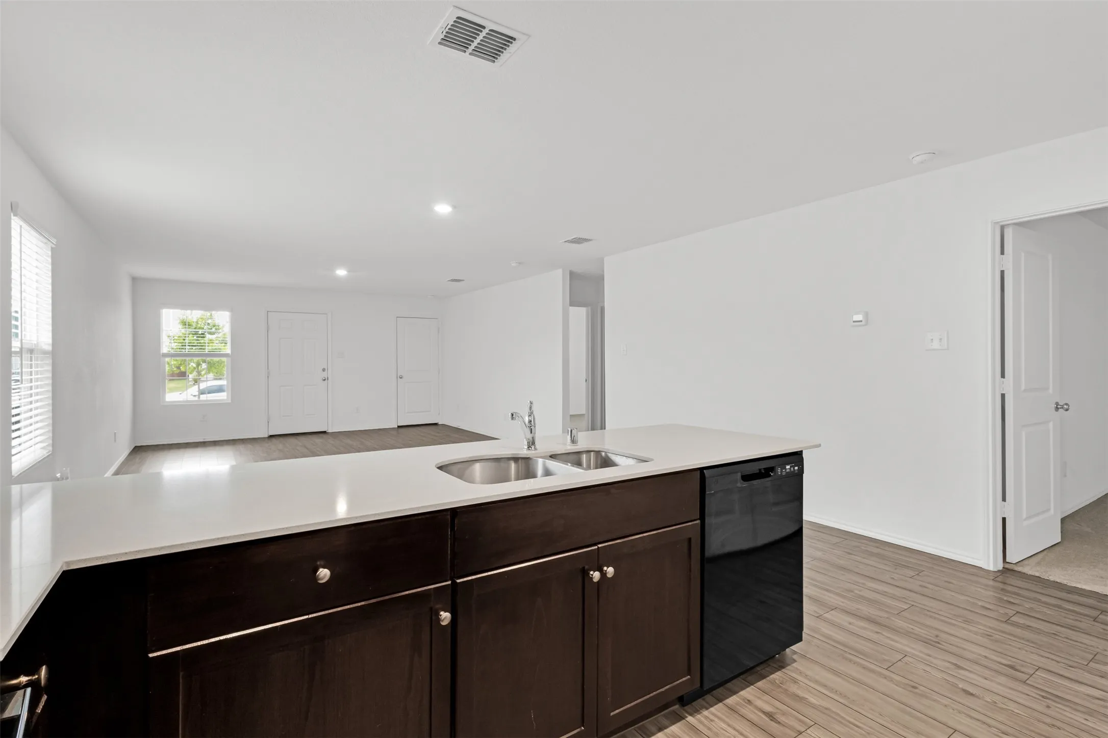 Open-concept kitchen featuring a dark wood cabinetry island with stainless steel appliances, white quartz countertops, and a large waterfall-edge countertop peninsula