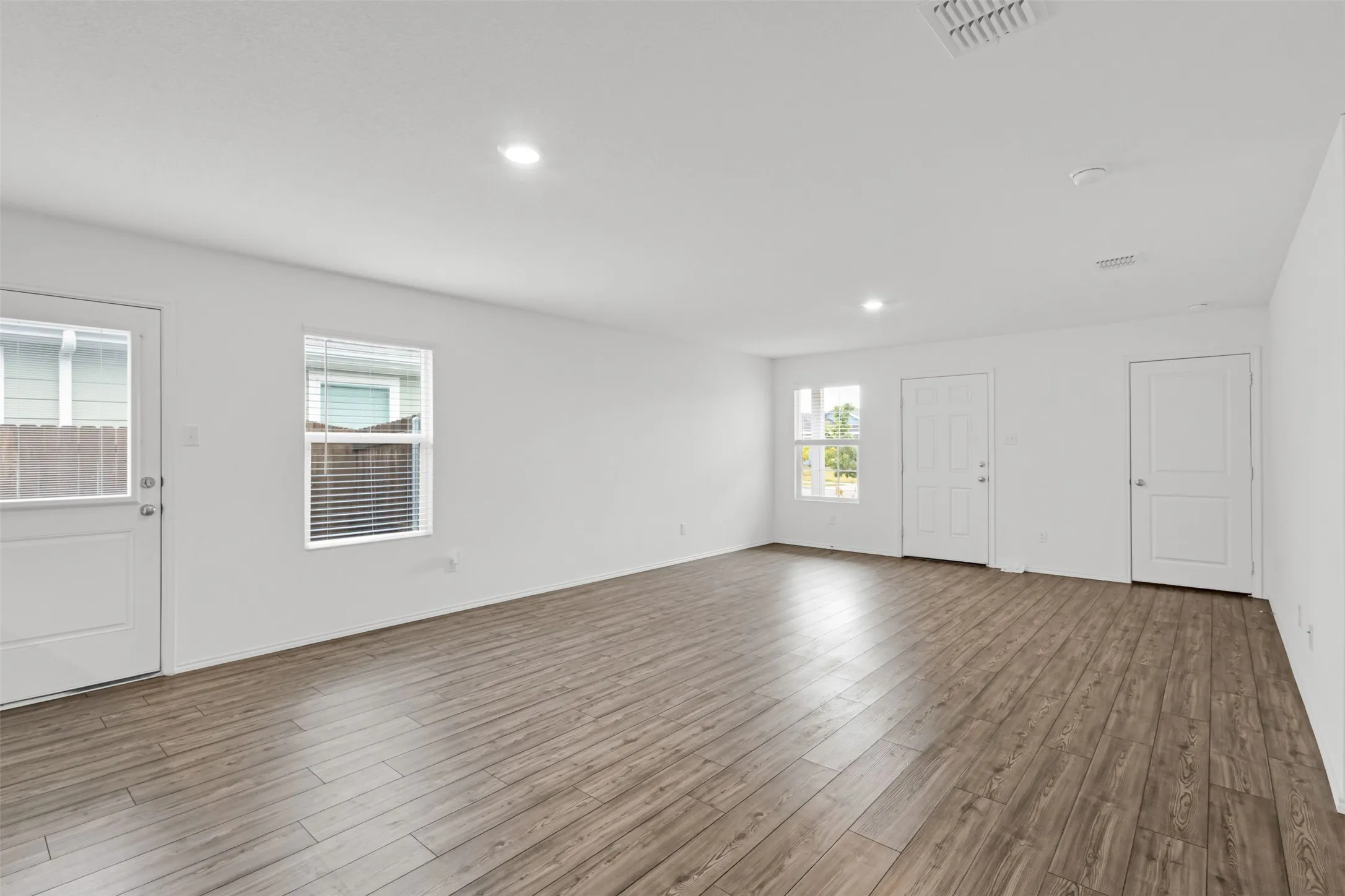 Open-concept living area featuring wood-finish flooring, recessed lighting, and multiple windows with blinds