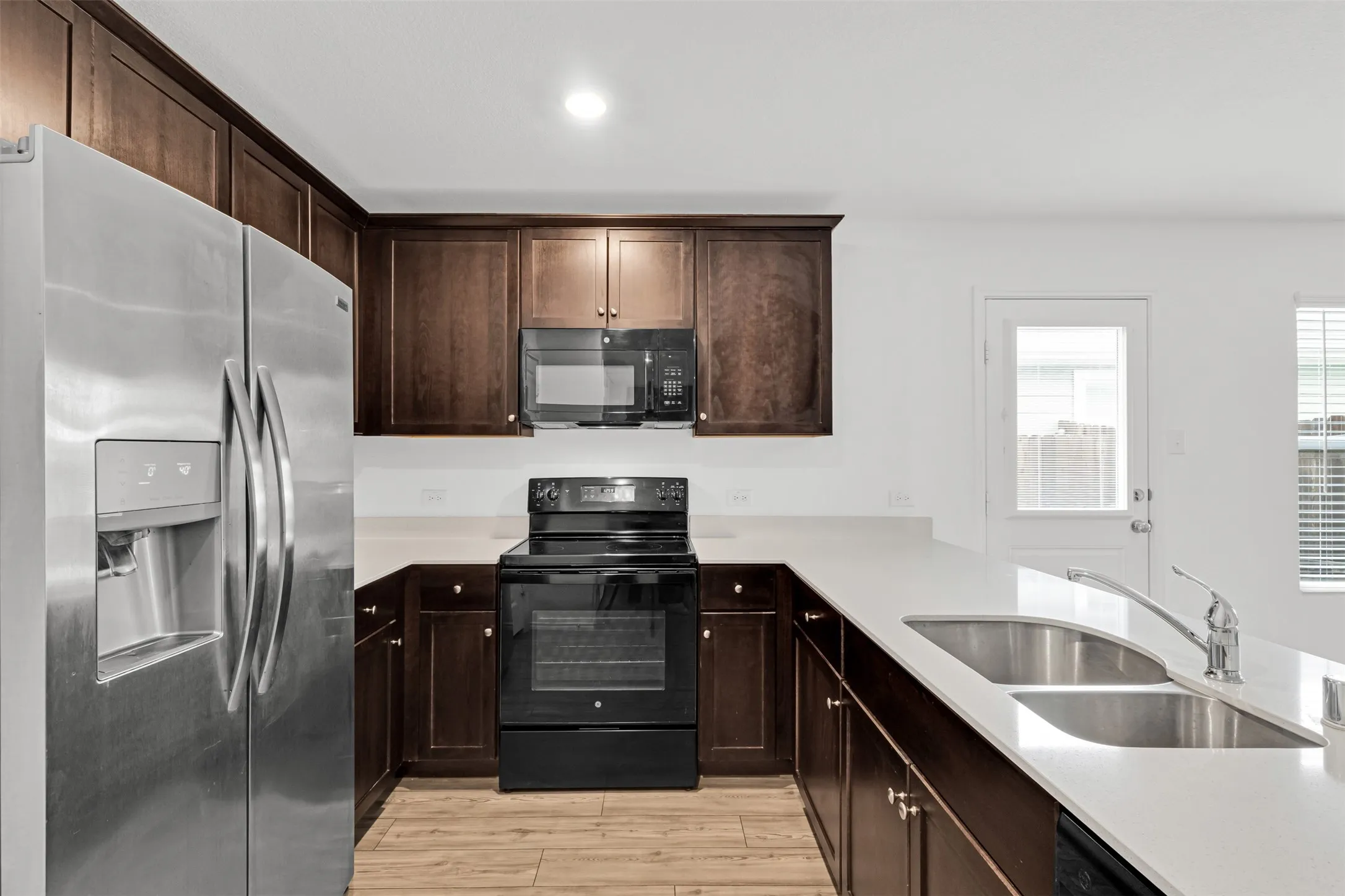 Kitchen featuring stainless steel appliances, dark wood-finish cabinetry, light-toned countertops, and wood-finish flooring