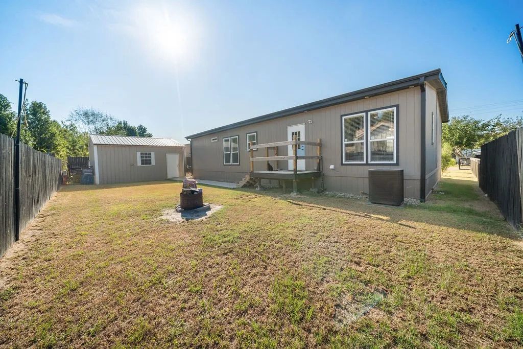 Expansive backyard featuring a detached storage shed, privacy fencing, and a raised wooden deck with railings