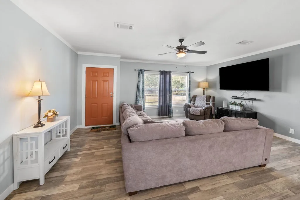 Wood-finish flooring, ceiling fan, crown molding, and a paneled entry door