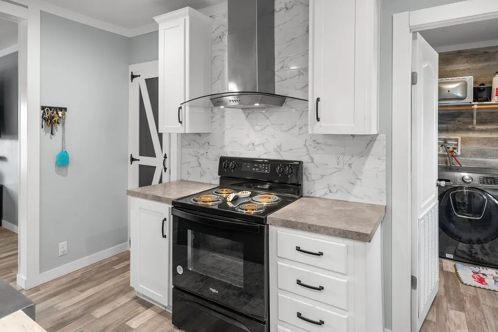 White cabinetry with black hardware, black range, stainless steel range hood, stone-finish countertops, and white marbled tile backsplash