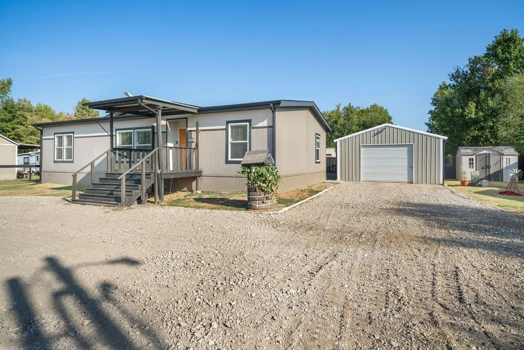 Exterior featuring a covered porch, gravel driveway, detached metal garage, and additional storage shed