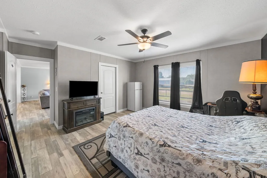 Wood-finish flooring, ceiling fan with integrated lighting, two windows with blinds, and a built-in fireplace console