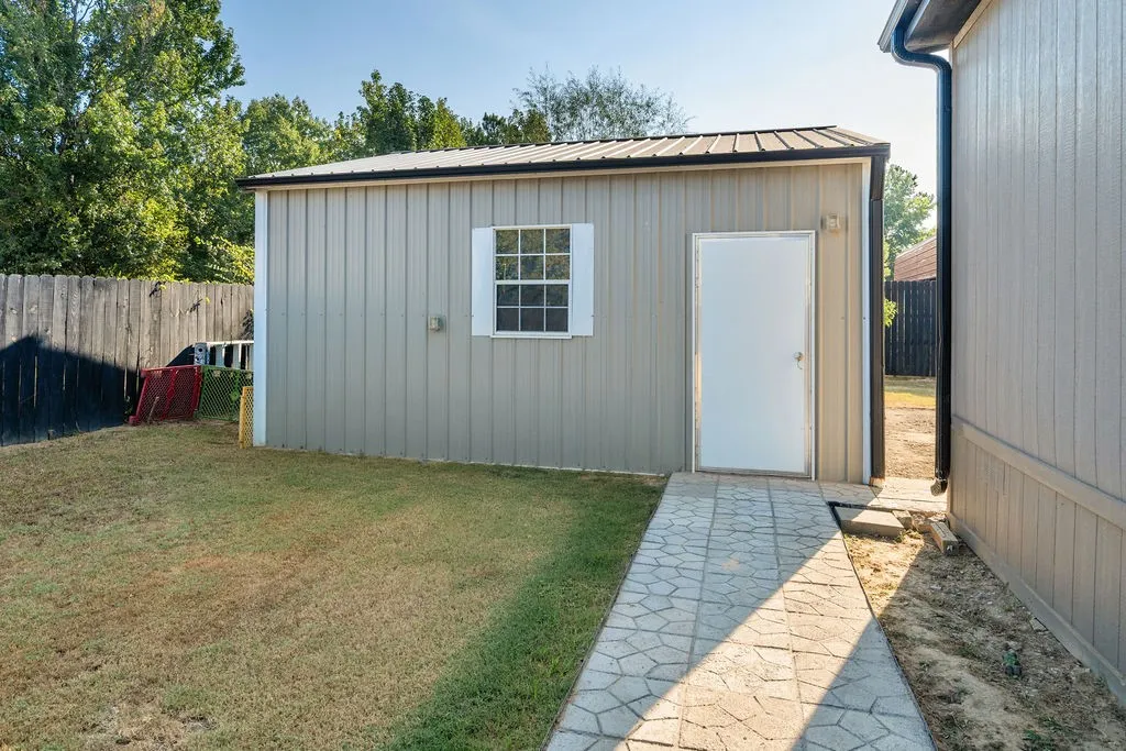 Detached metal-sided structure with a metal roof, a multi-pane window, and a white entry door, complimented by a patterned concrete pathway
