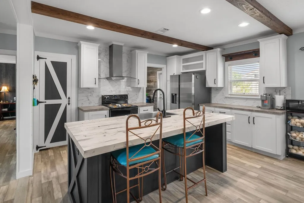 Modern kitchen featuring wood-finish flooring, white cabinetry, a central island with a light-toned countertop, stainless steel appliances, and exposed wood beams