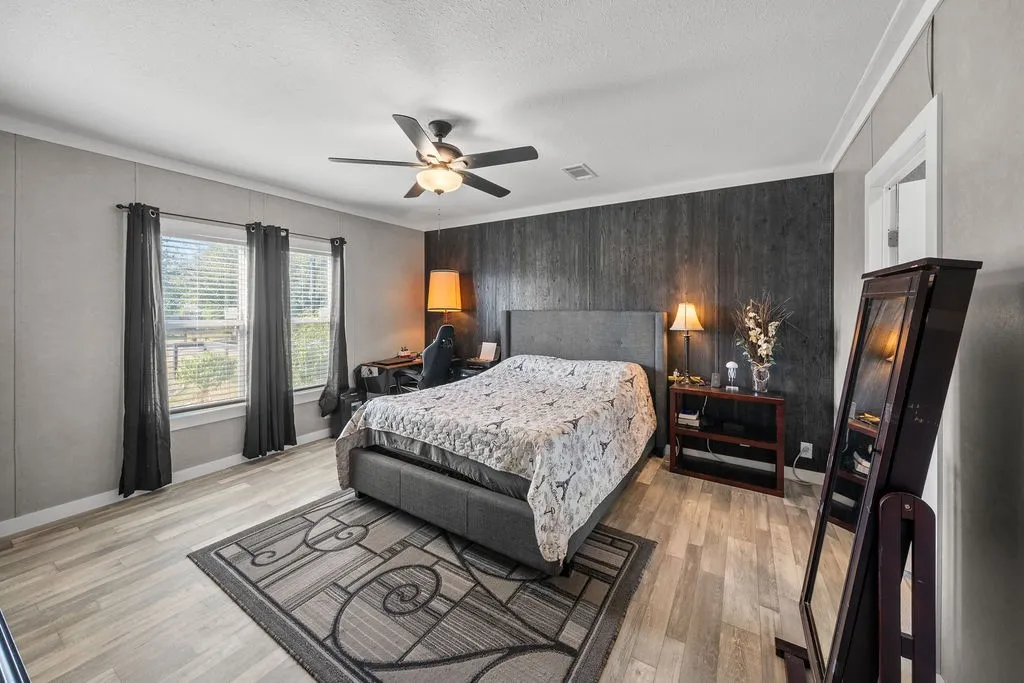 Wood-finish flooring, accent wall, ceiling fan with integrated lighting, multiple windows, and crown molding